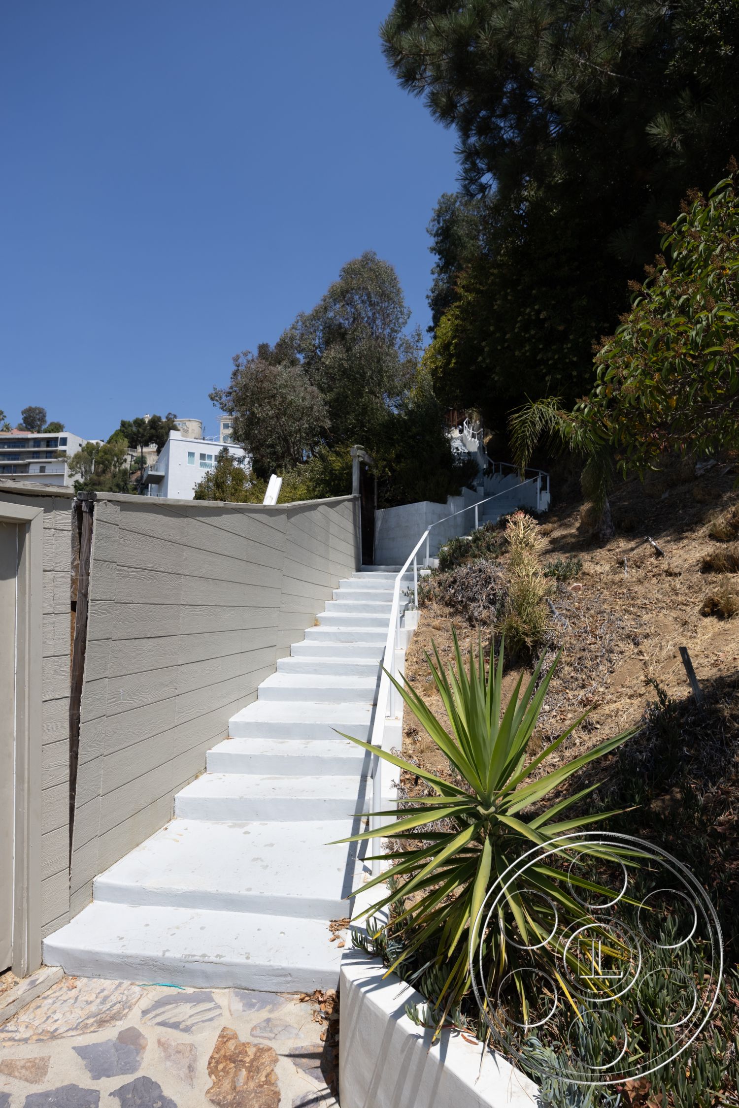 Retro 294 - natural stone retaining wall, textured plaster wall, exterior stone pathway, exterior concrete steps, exterior painted wood siding, minimalist landscaped garden, modern plantings, steep hillside location, curved stair design, sleek white railing