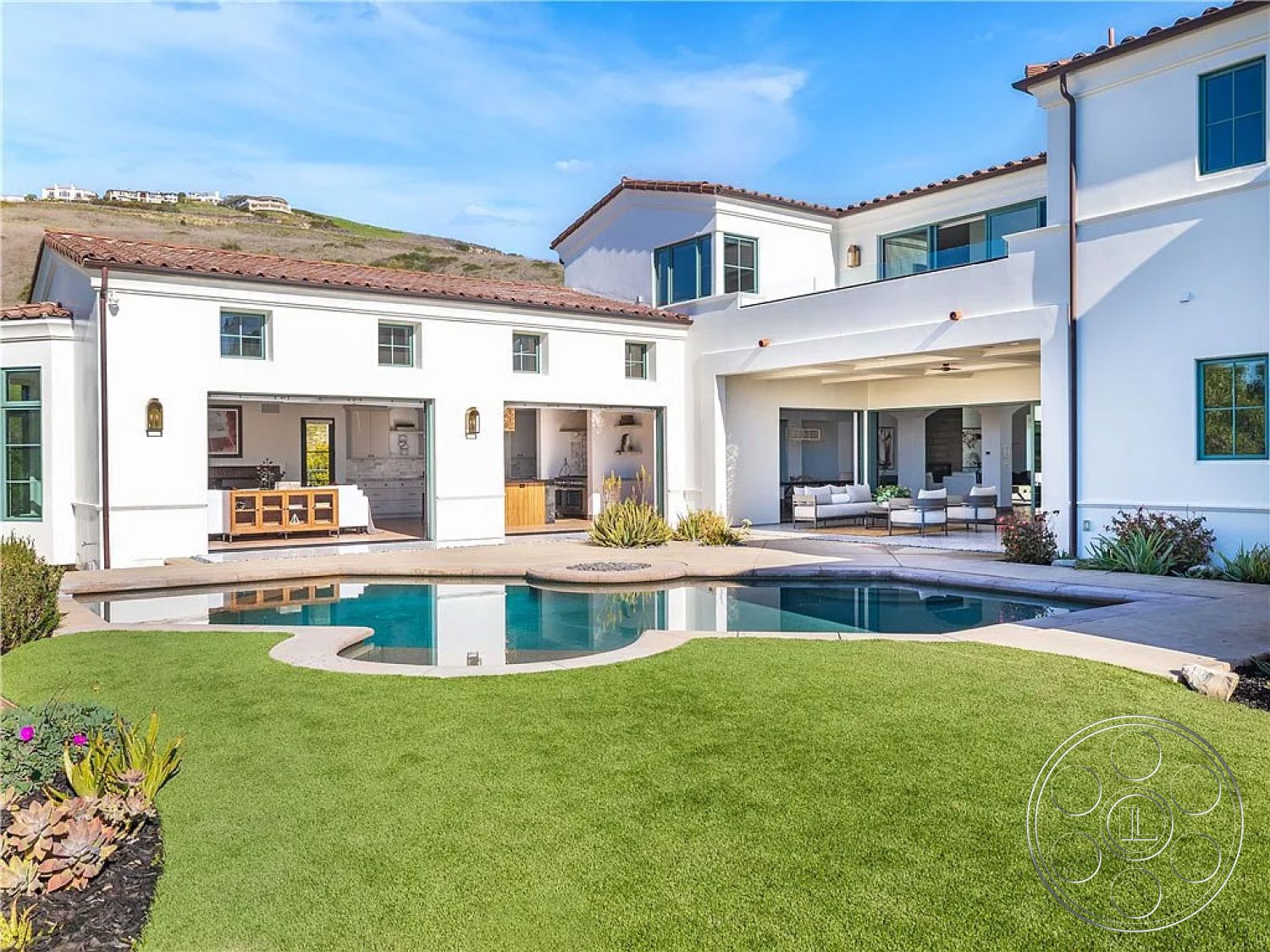 Spanish 167 - glass sliding doors, rectangular swimming pool, floor-to-ceiling windows, modern landscape design, concrete walkway, arched doorways, concrete pool deck, artificial turf lawn, outdoor living area, stucco exterior walls, open-concept kitchen, wooden kitchen cabinets, suburban backyard setting, outdoor lounge seating, steel light fixtures, stone garden border, tile roof with terracotta shingles, covered patio area, desert mountain backdrop, integrated outdoor kitchen, landscaped gardens with succulents