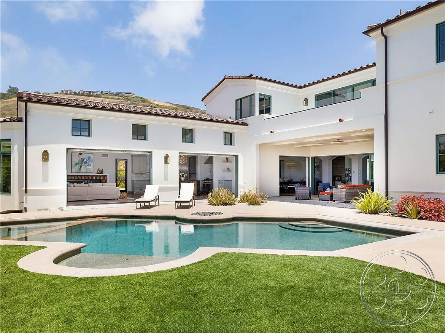 Spanish 167 - exterior, landscaped garden, natural stone accents, white stucco walls, glass sliding doors, outdoor seating area, rectangular swimming pool, floor-to-ceiling windows, paved walkway, hillside view, red tile roof, concrete pool deck, modern Mediterranean architecture, open patio space, grassy backyard, illuminated wall sconces, urban outskirts setting