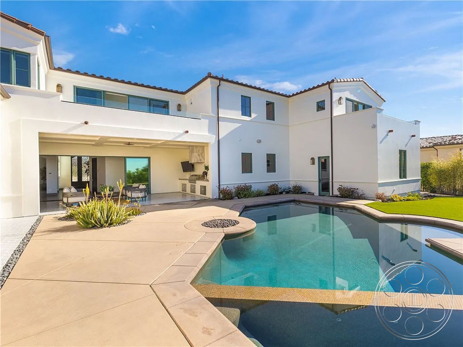 Spanish 167 - exterior concrete pool border, exterior shaded patio area, exterior sliding glass doors, exterior black window frames, exterior rectangular pool, interior open-concept living area, interior glass sliding doors, exterior outdoor seating area, interior spacious floor plan, exterior stone landscaping, exterior tan concrete patio floor, exterior green lawn, exterior modern white stucco walls, interior outdoor kitchen area, exterior desert landscape
