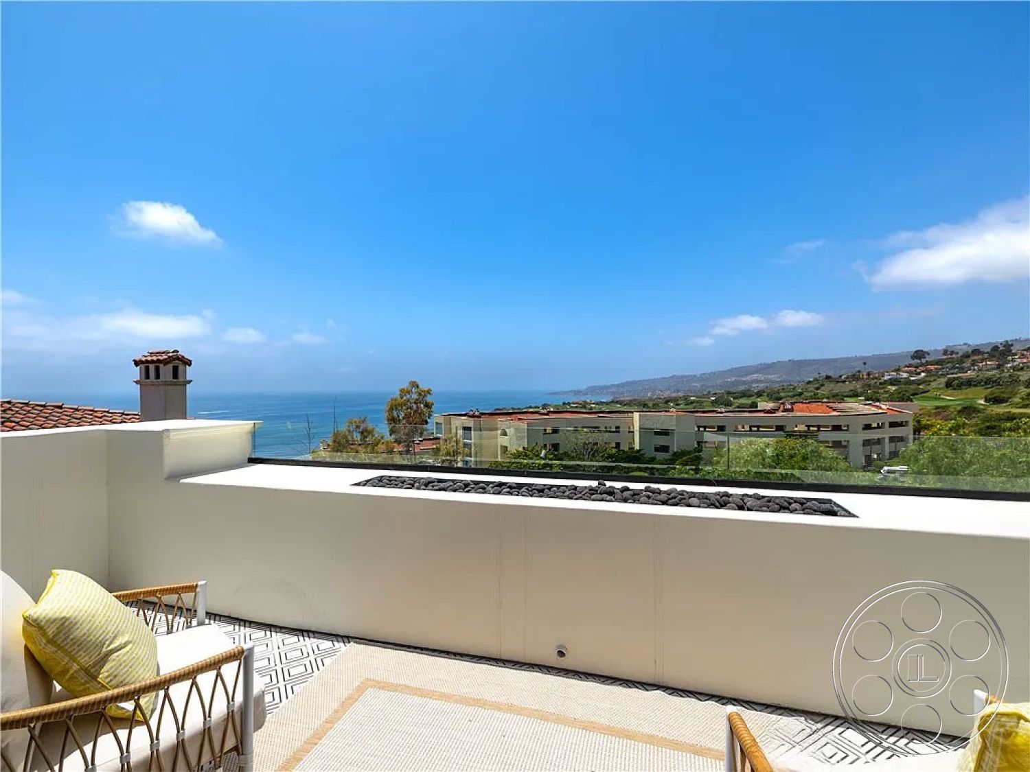 Spanish 167 - white stucco walls, terracotta roof tiles, contemporary outdoor living space, natural light exposure, modern outdoor seating area, oceanfront property, exterior ocean view balcony, textured stone tile flooring, glass railing for unobstructed view, decorative outdoor cushions, fire feature with natural stone, surrounding coastal landscape, urban beachfront setting, patio with geometric tile design, lush green hill backdrop