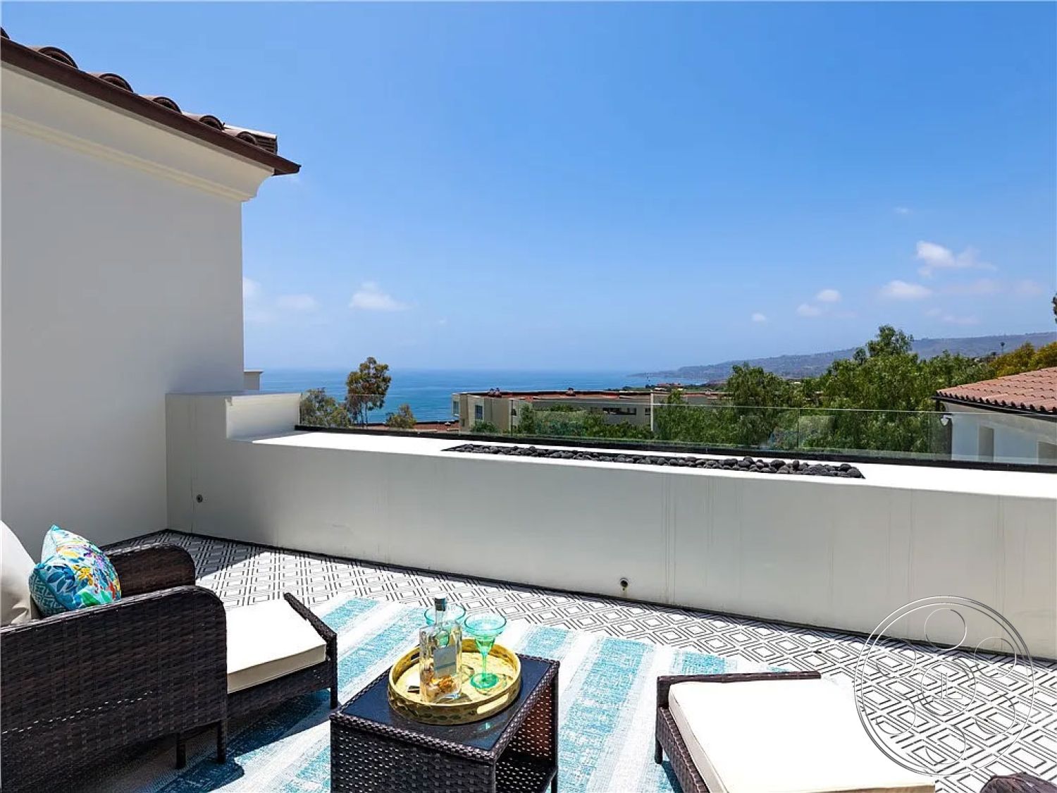 Spanish 167 - glass railing, outdoor lounge area, potted greenery, contemporary outdoor space, stylish outdoor decor, decorative outdoor rug, woven outdoor seating, exterior terrace view, modern tile patio flooring, coastal ocean view, ceramic tile pattern, sunny beach house setting