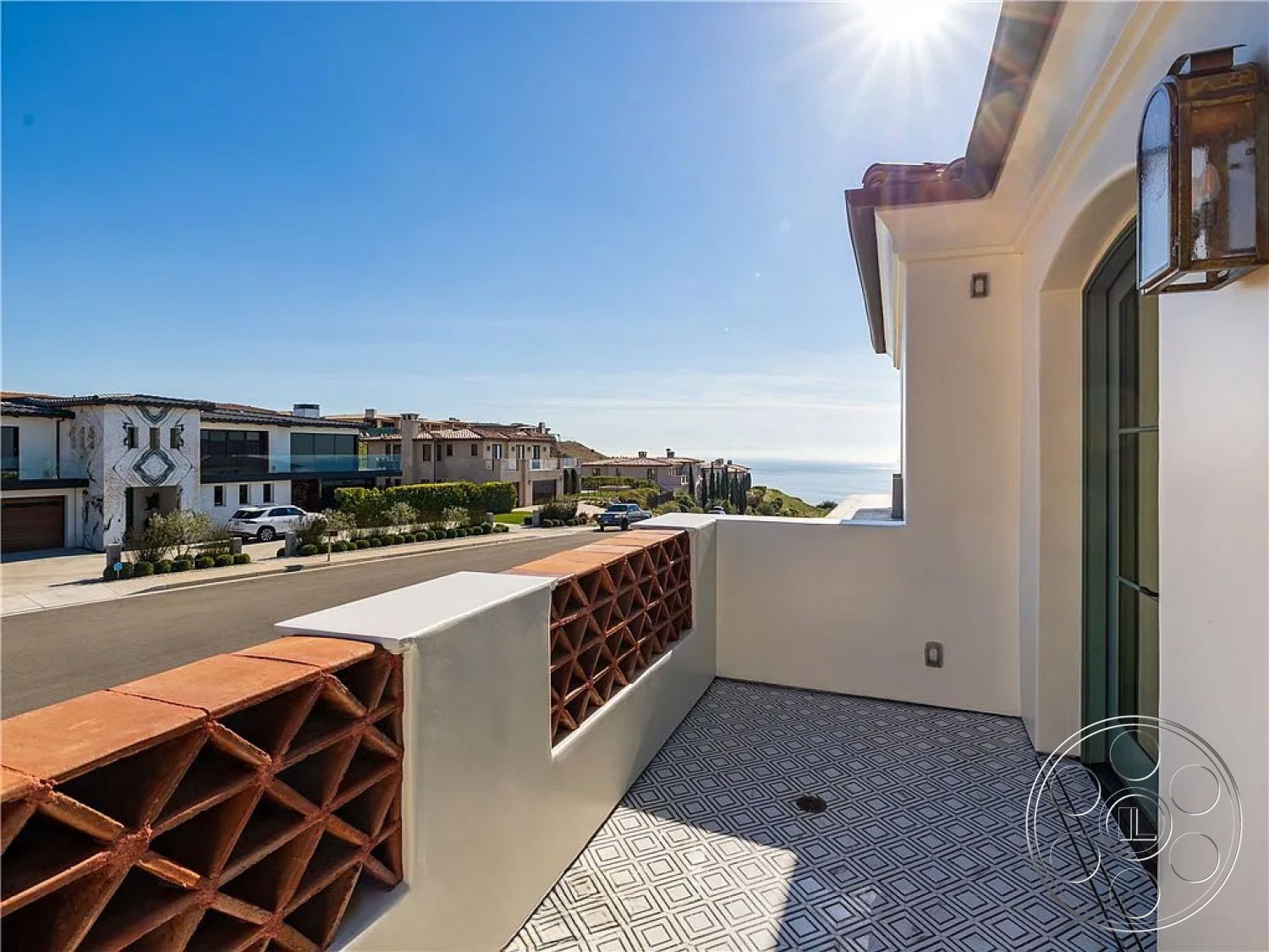 Spanish 167 - landscaped front yard, outdoor living space, modern architectural style, ocean view, white stucco exterior, front porch area, decorative wrought iron lanterns, horizontal wood siding accents, terracotta block balcony wall, geometric patterned tile flooring, exposed natural light, residential neighborhood setting, curved balcony design, clear glass window frames, smooth plaster wall treatment, coastal climate environment