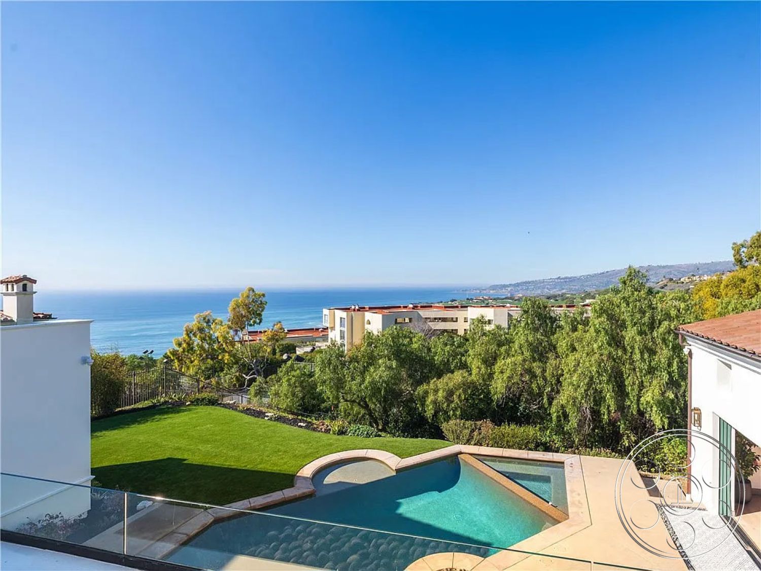 Spanish 167 - modern architectural lines, lush green lawn, outdoor living area, open-air concept, curved pool shape, concrete pool patio, white stucco exterior walls, glass railing terrace, tile roof with terracotta shingles, rectangle infinity pool, landscaped garden surrounding pool, expansive ocean view, elevated seaside lot, exterior minimalistic design, cleared hillside surroundings, large glass doors opening to terrace, natural stone pool border, contemporary exterior styling, landscaped backyard space, coastal dwelling