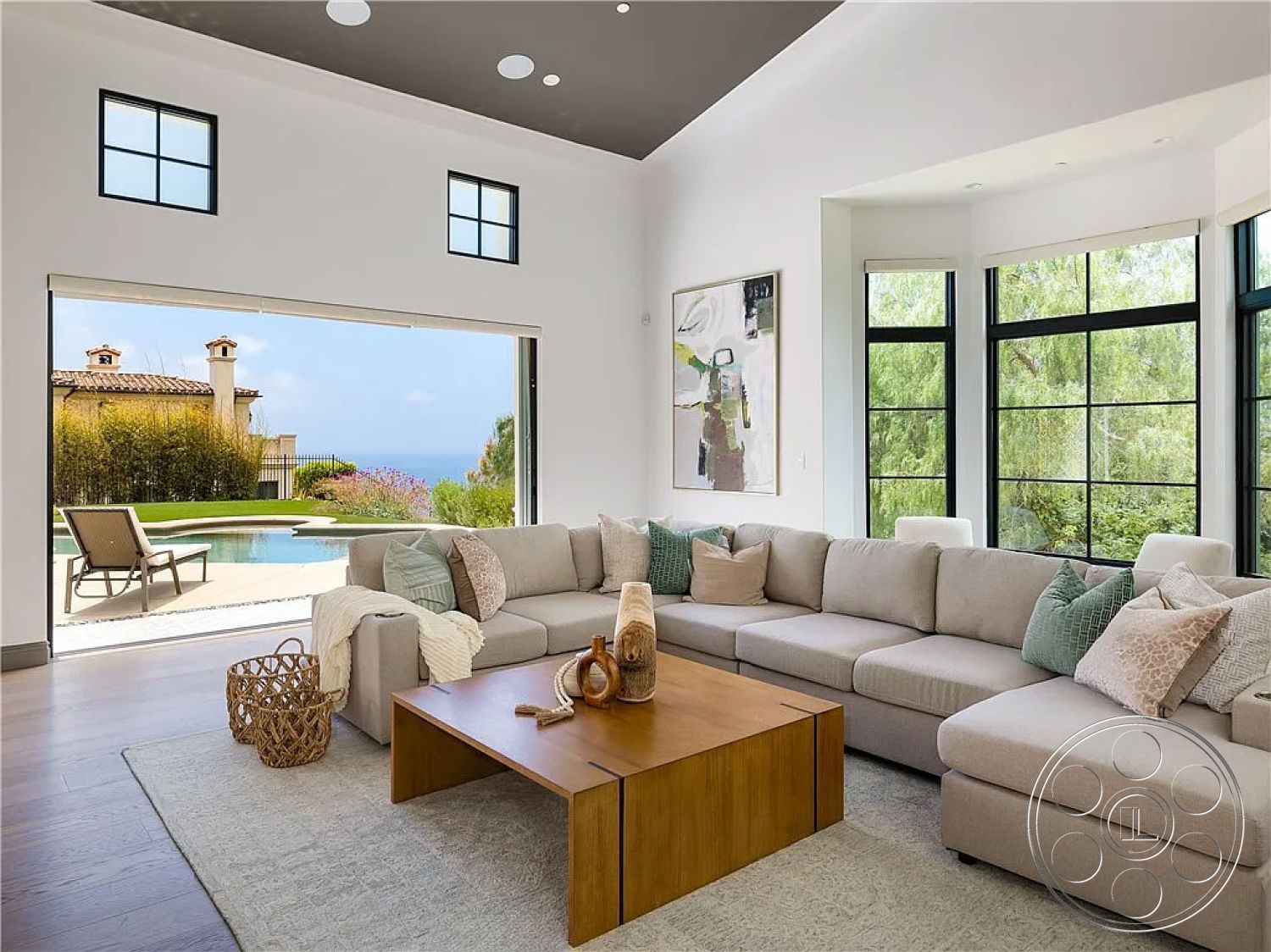 Spanish 167 - decorative area rug, open concept design, curved wall design, sunny coastal setting, modern wooden coffee table, hardwood flooring in living room, minimalist wall art, contemporary sectional sofa, textured white plaster walls, interior living room with vaulted ceiling, glass sliding doors to exterior pool area, large windows with black steel frames, neutral color palette with pastel accents, outdoor pool view from interior space, horizontal landscaping in background, natural light flooding the room, architectural details with recessed lighting, glass partition between indoor and outdoor