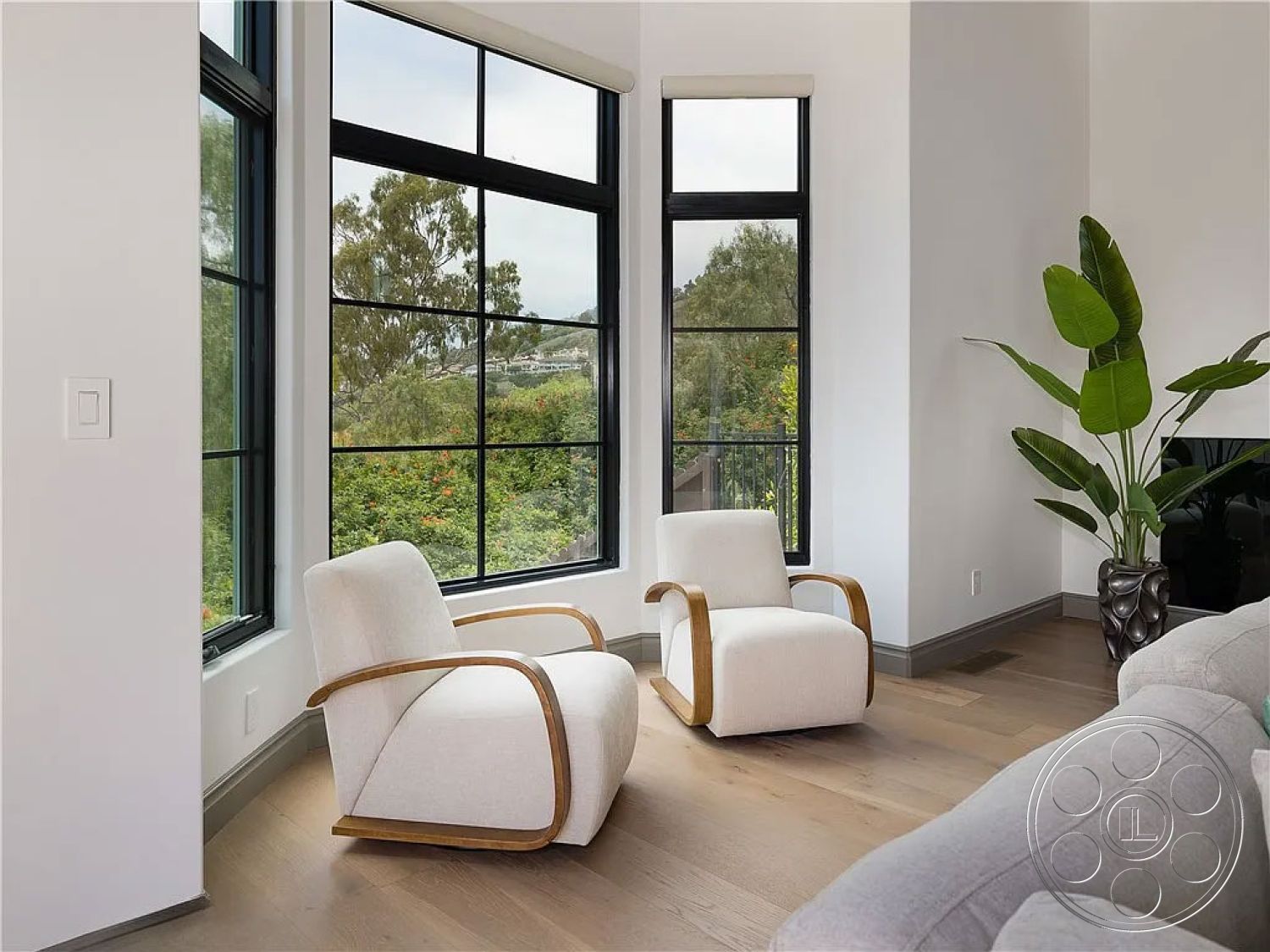 Spanish 167 - neutral color palette, open space layout, architectural details, comfortable seating area, contemporary interior design, large black framed windows, hardwood flooring living room, white painted walls interior, light and airy ambiance, indoor potted plant, natural light-filled room, clean lines architectural style, modern minimalist armchairs, curved wood accents on seating, view of landscaped garden