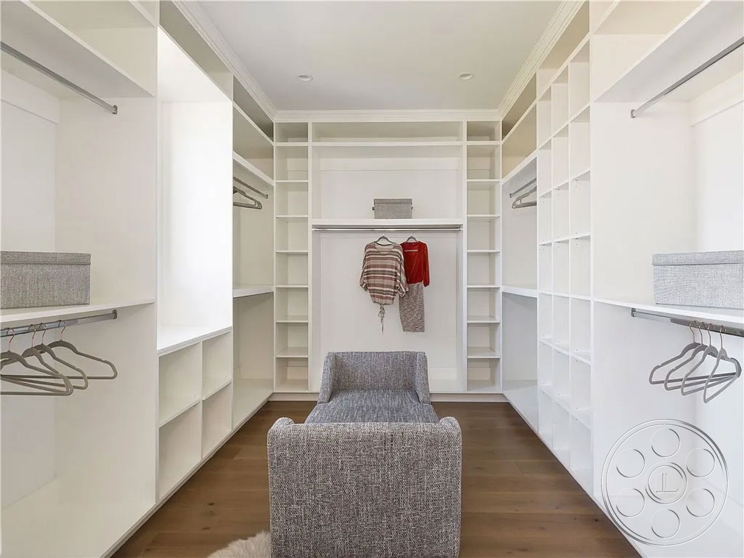Spanish 167 - neutral color palette, hardwood flooring, white built-in shelving, natural light from windows, cozy armchair, functional design elements, modern minimalist design, crisp white walls, interior walk-in closet, open storage solutions, hanging space with clothing, organized clothing storage
