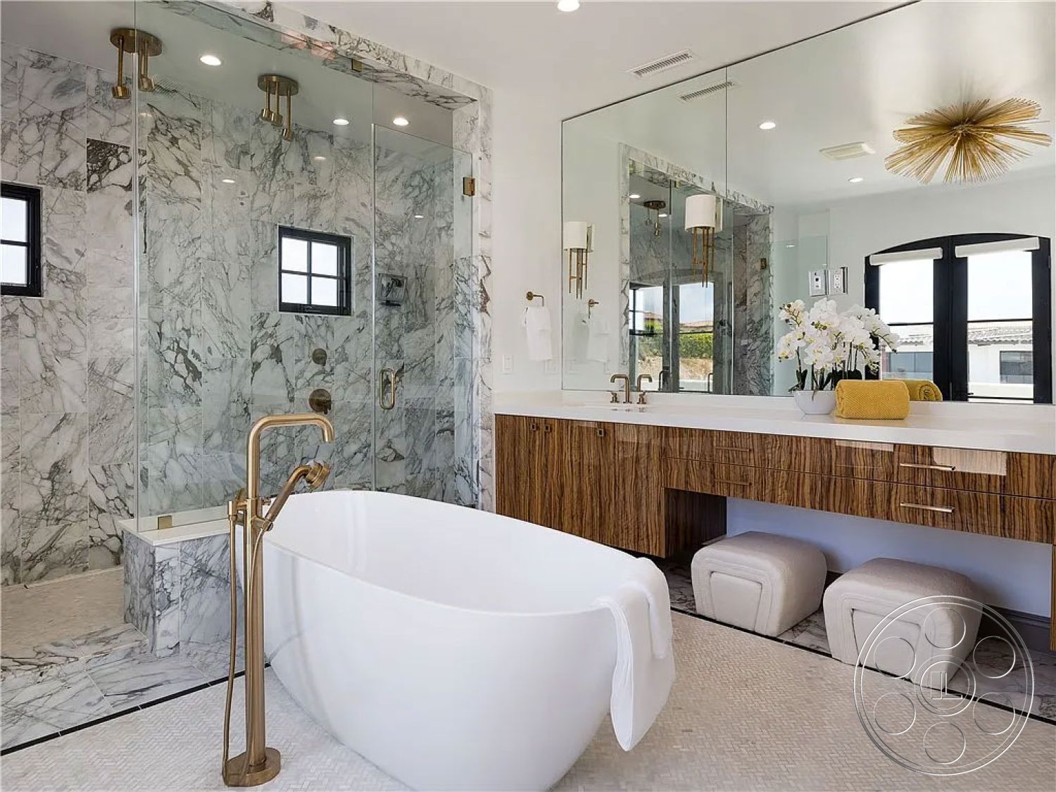 Spanish 167 - neutral color palette, textured area rug, glass shower enclosure, open space layout, minimalist design elements, modern pendant lighting, marble flooring, natural light from windows, dual sink vanity, interior bathroom design, freestanding soaking tub, large format marble tiles, marble shower walls, luxurious spa-like atmosphere, brass floor-mounted tub faucet, wood vanity with horizontal grain, mirrored backsplash, white ceramic towels, oval bathtub shape, contemporary bathroom fixtures, stylish countertop accessories