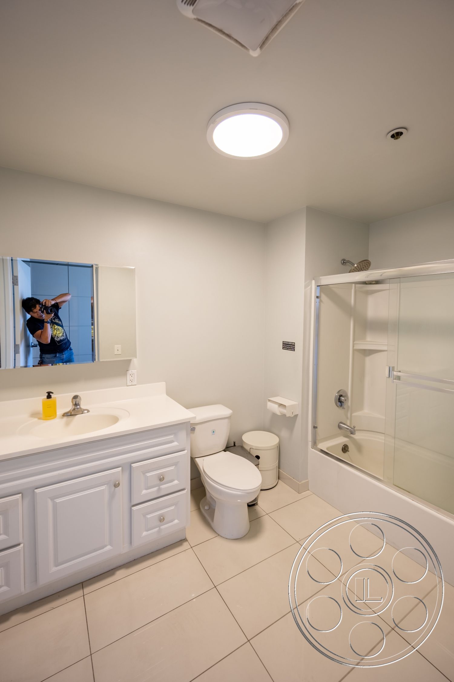 Loft 158 - clean lines, minimalist design, functional layout, bright lighting, white toilet, neutral color scheme, easy maintenance materials, glass shower doors, interior bathroom, chrome faucet fixtures, white painted walls, modern ceiling light fixture, glazed ceramic tile flooring, white vanity cabinet, rectangle vanity mirror, bathtub with shower