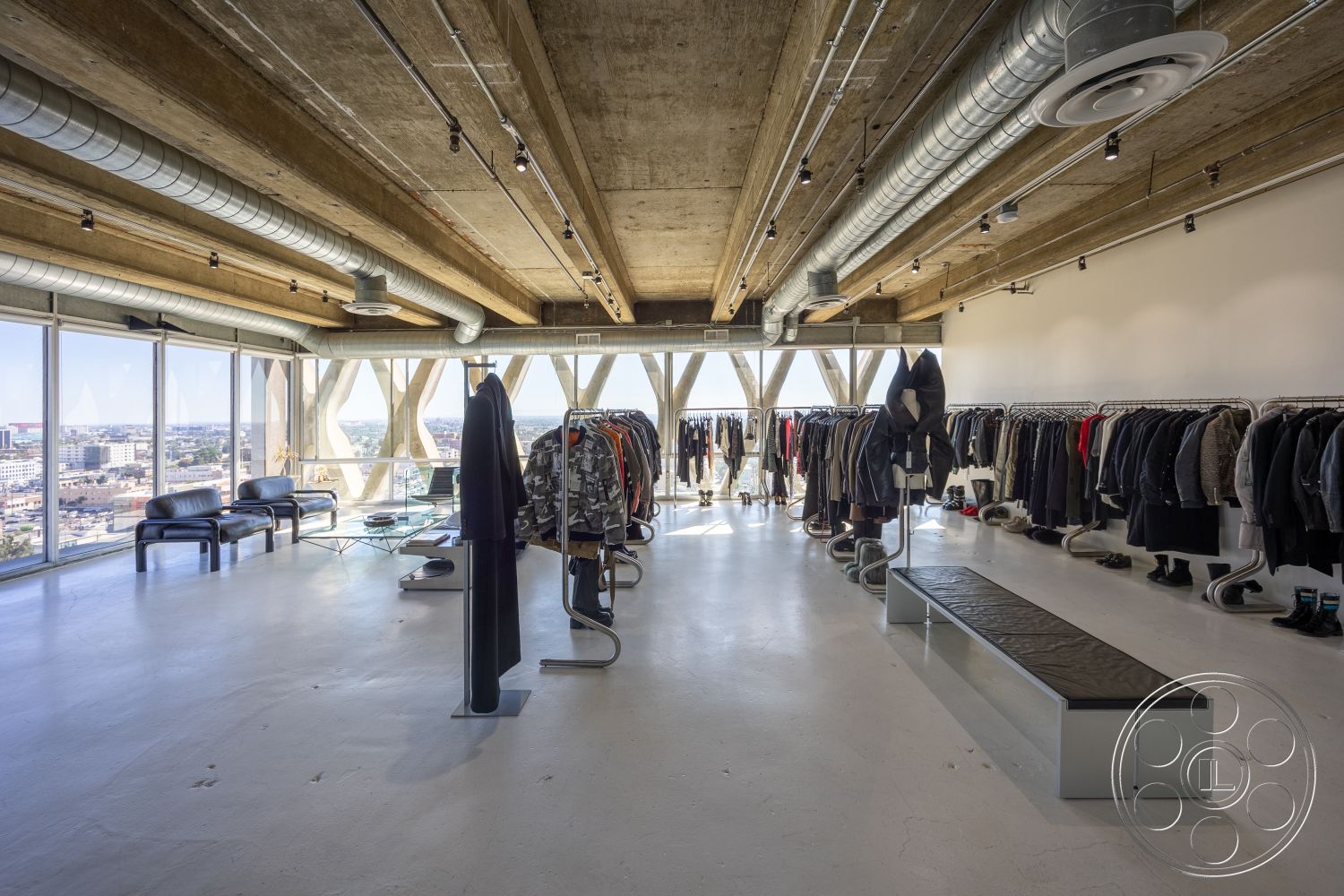 Loft 159 - spacious layout, polished concrete flooring, floor-to-ceiling glass windows, industrial-style lighting fixtures, modern contemporary design, urban city skyline view, exposed concrete ceiling beams, open-plan retail space, minimalistic black leather seating, metal garment racks, transparent glass display table, interior clothing showroom, suspended ductwork ceiling, architectural concrete walls, furniture-free floor space for movement