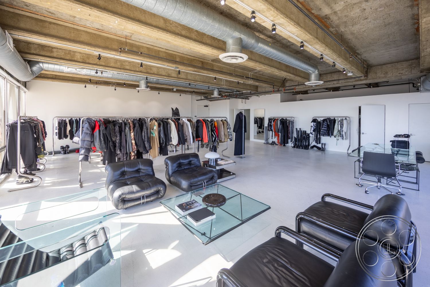 Loft 159 - natural light, contemporary design, open layout, concrete floor, glass coffee table, city view, urban setting, strip lighting, exposed concrete ceiling, glass mirror, retail space, white painted walls, minimalist interior, metal clothing racks, industrial ceiling ductwork, leather lounge chairs, fashion showroom