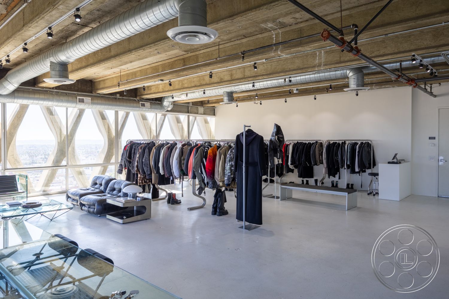 Loft 159 - minimalist aesthetic, polished concrete flooring, modern furnishings, open concept layout, urban skyline view, exposed concrete ceiling, metal ductwork, natural light exposure, steel frame construction, glass storefront windows, commercial space design, industrial style design, clothing display rack, metallic accent bench, high-rise interior, retail showroom layout