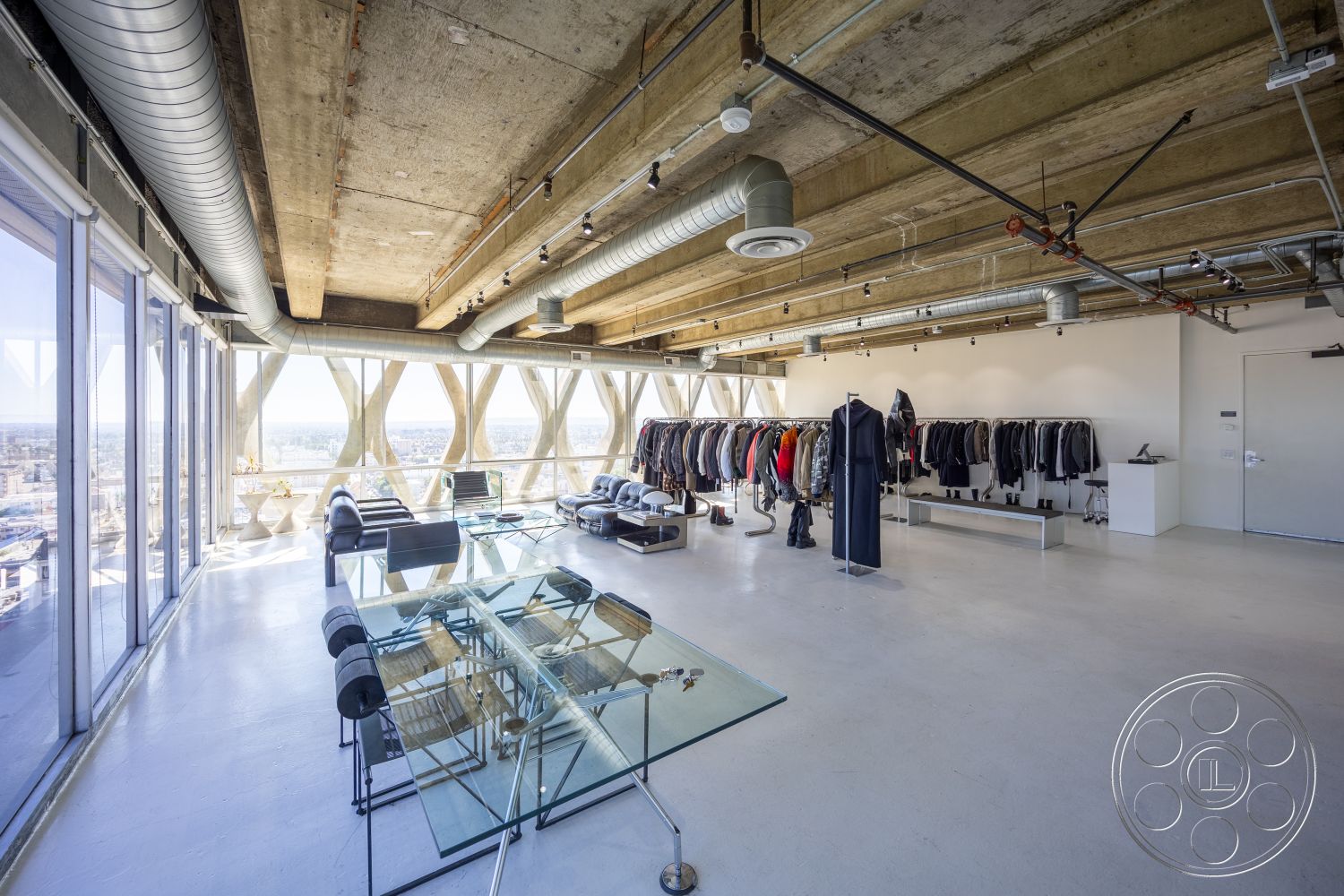 Loft 159 - high ceilings, concrete floor, exposed concrete ceiling, contemporary lighting fixtures, modern minimalist design, open floor plan interior, industrial style decor, glass conference table, leather sofa seating, large panoramic windows, metallic ductwork, fashion retail display area, urban city view setting, steel and glass accents
