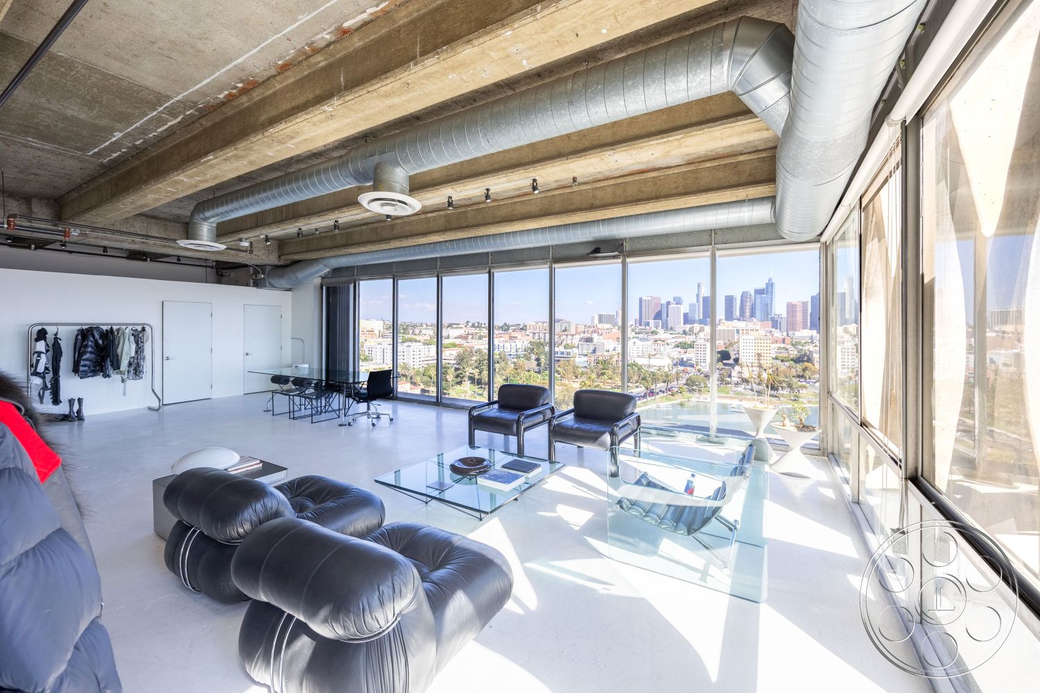 Loft 159 - polished concrete flooring, urban skyline view, mid-century modern furniture, exposed concrete ceiling, metal framed chairs, minimalist interior design, open floor plan layout, natural light emphasis, exposed brick accent wall, industrial style decor, contemporary artwork display, steel ductwork, glass wall windows, transparent glass coffee table, interior loft setting, sleeve-style clothing rack
