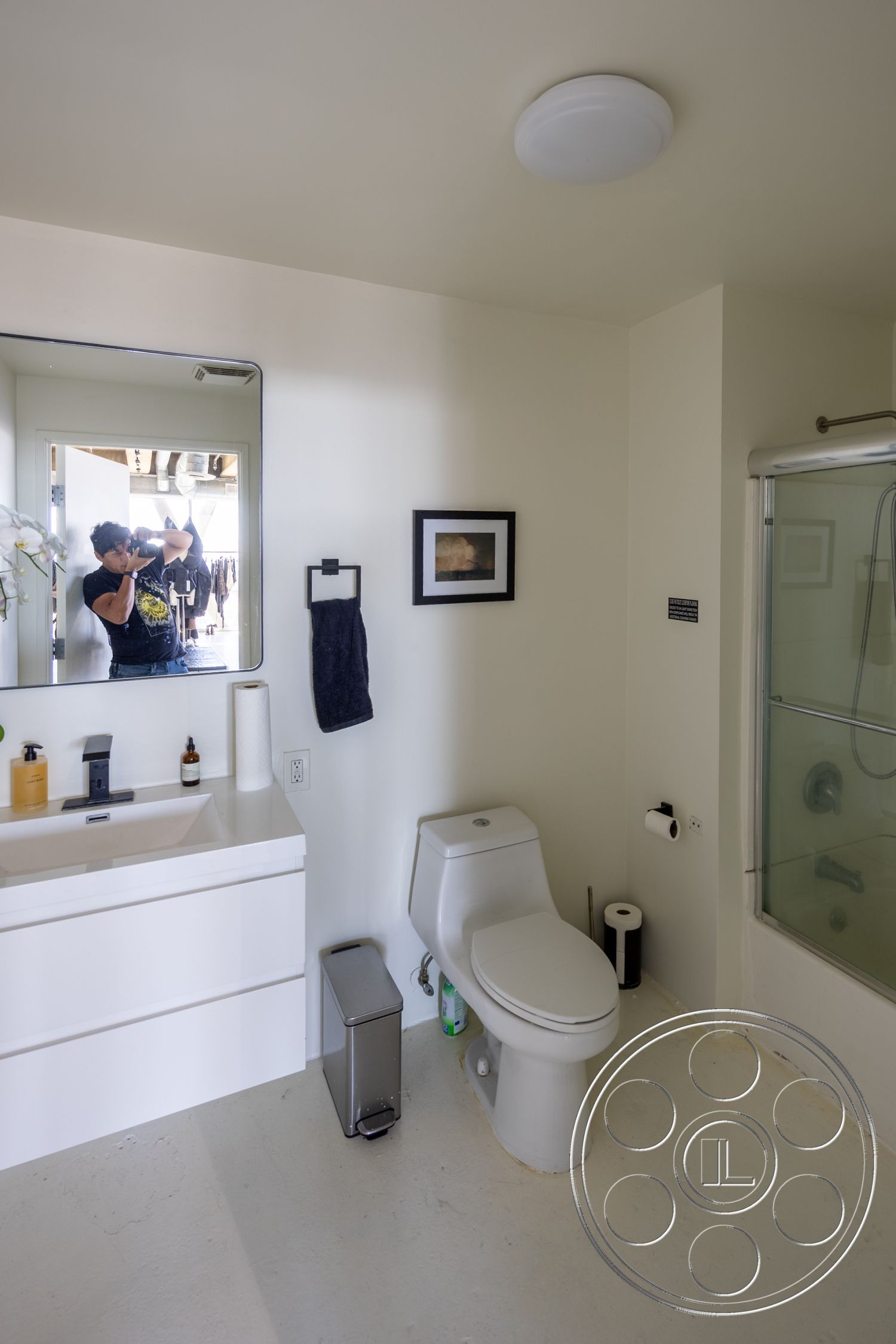 Loft 159 - neutral color palette, natural light, concrete flooring, framed wall art, under-sink storage, minimalist bathroom design, interior bathroom, white painted walls, modern faucet fixtures, floating bathroom vanity, transparent glass shower enclosure, toilet paper holder, towel bar with dark towel, sliding bathroom door, white ceiling light fixture