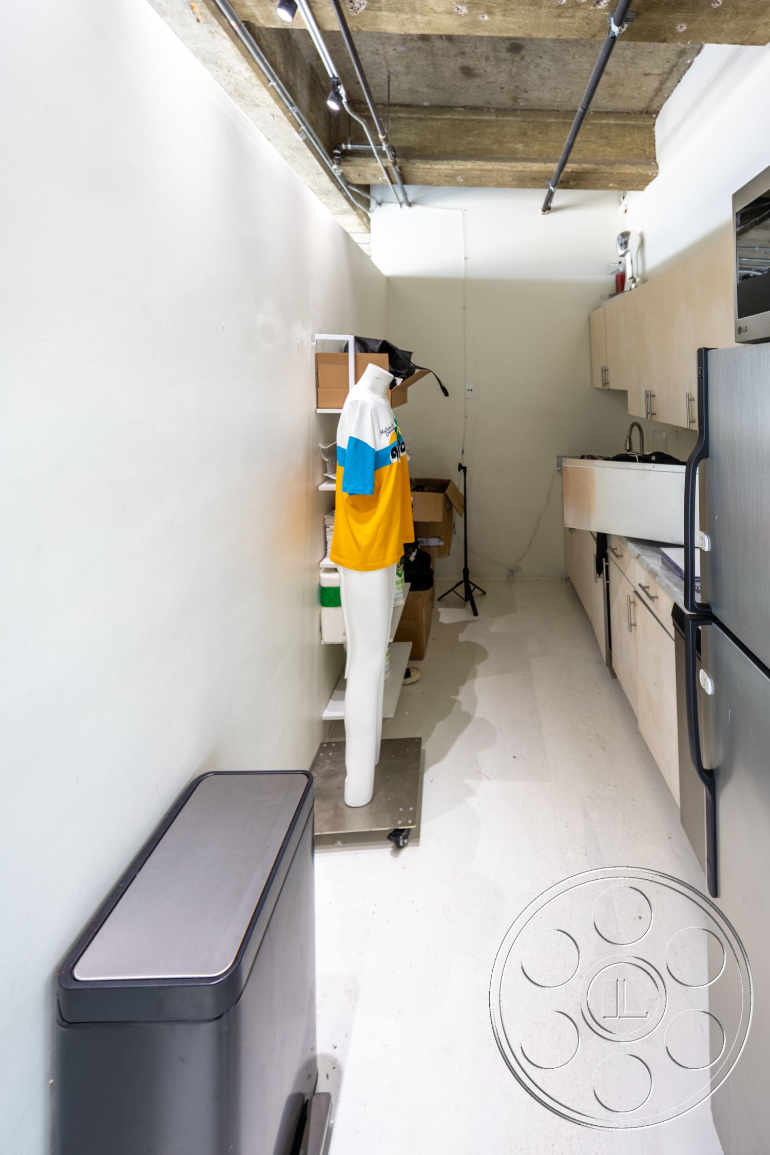 Loft 159 - open floor plan, stainless steel refrigerator, vinyl flooring, modern kitchen appliances, white painted walls, industrial-style lighting, exposed concrete ceiling panels, metal storage shelves, mannequin display stand, black kitchen trash bin