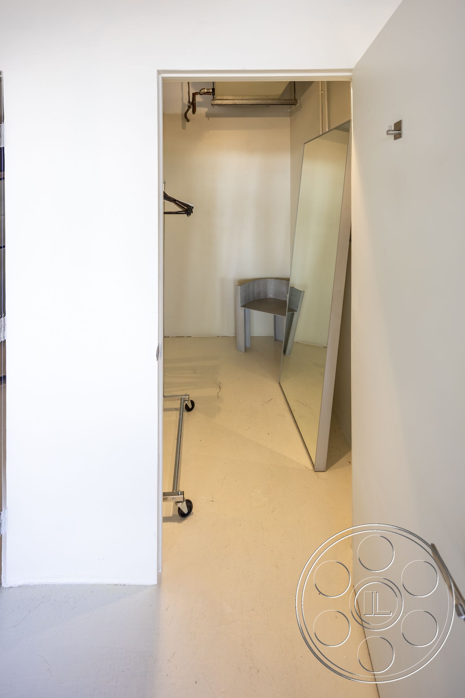 Loft 159 - neutral color palette, modern design, concrete flooring, minimalist style, stylish storage solutions, full-length mirror, white painted walls, single-door entry, hanging clothing rack, simple chair design, open closet space, industrial pipe ceiling detail, functional dressing area
