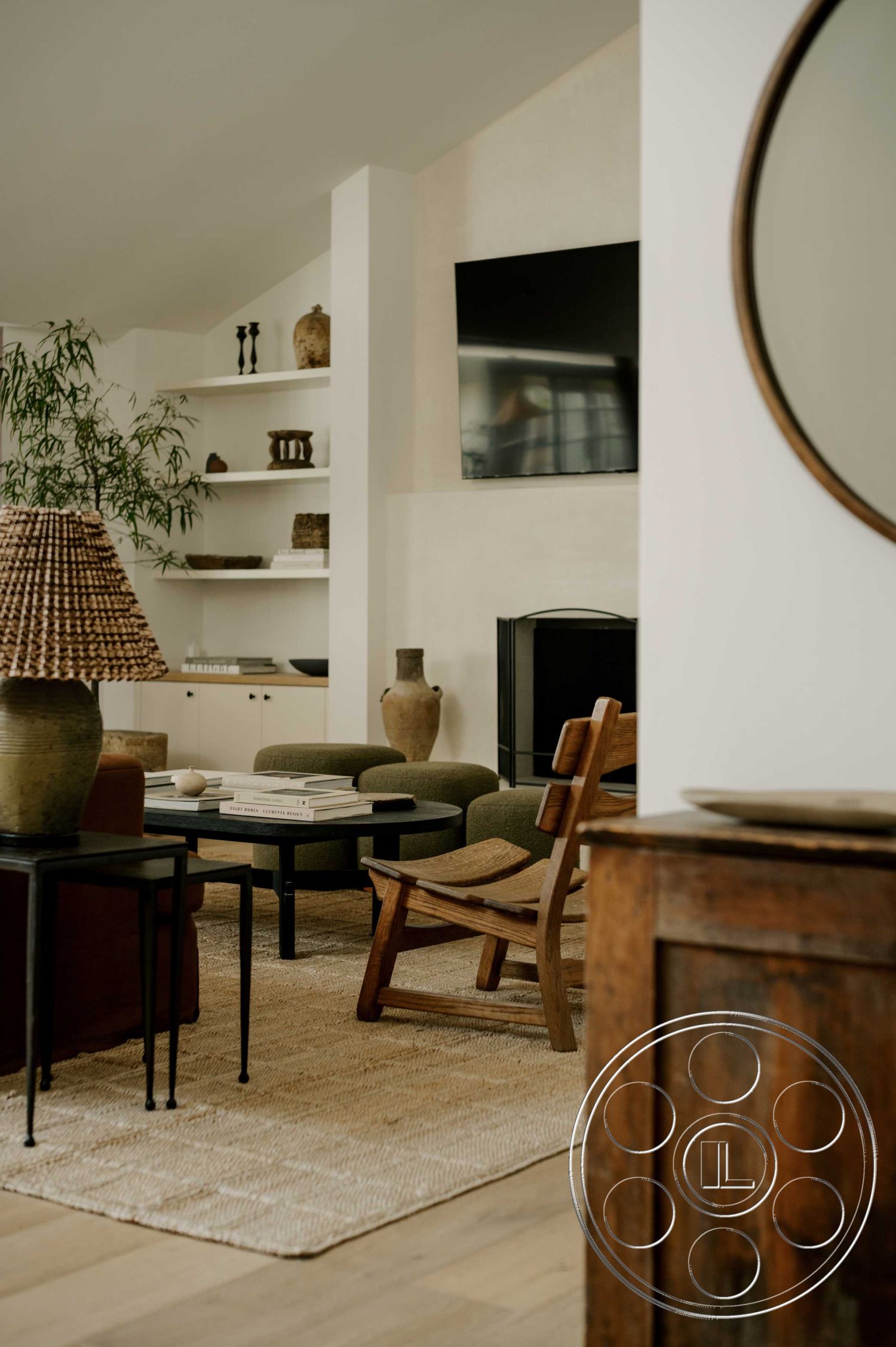 Americana 429 - large flat-screen television, contemporary coffee table, earth-toned color palette, woven pendant light fixture, natural fiber area rug, textured plaster wall finish, open shelving units, minimalist wall decor, softwood plank flooring, mid-century modern armchair, decorative ceramic vases, fabric upholstered seating, black metal side tables, wooden cabinet with rustic finish, houseplants in decorative pots, geometric shape elements, neutral tone accents