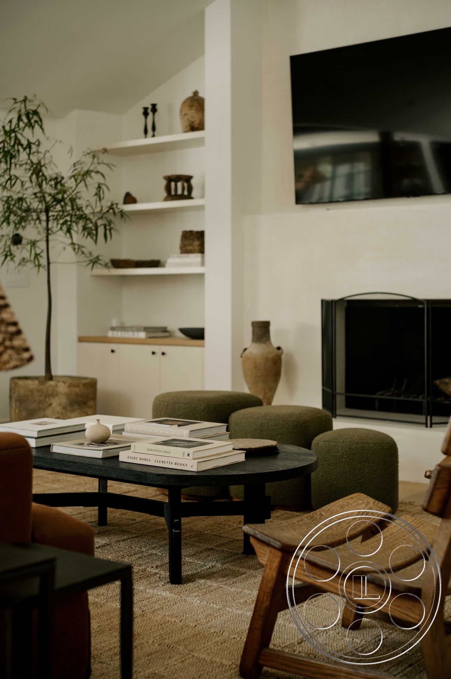 Americana 429 - natural light from large windows, cozy reading nook, sculptural lighting fixtures, mid-century modern design elements, built-in shelving units, modern accent decor, open floor plan living space, contemporary art display, exposed plaster walls, blackened wood coffee table, circular coffee table with wood base, textured area rug flooring, green upholstered accent chairs, neutral color palette decor, stone fireplace with black metal screen, earthy ceramic vases, plant decor for indoor greening, wood and metal accents