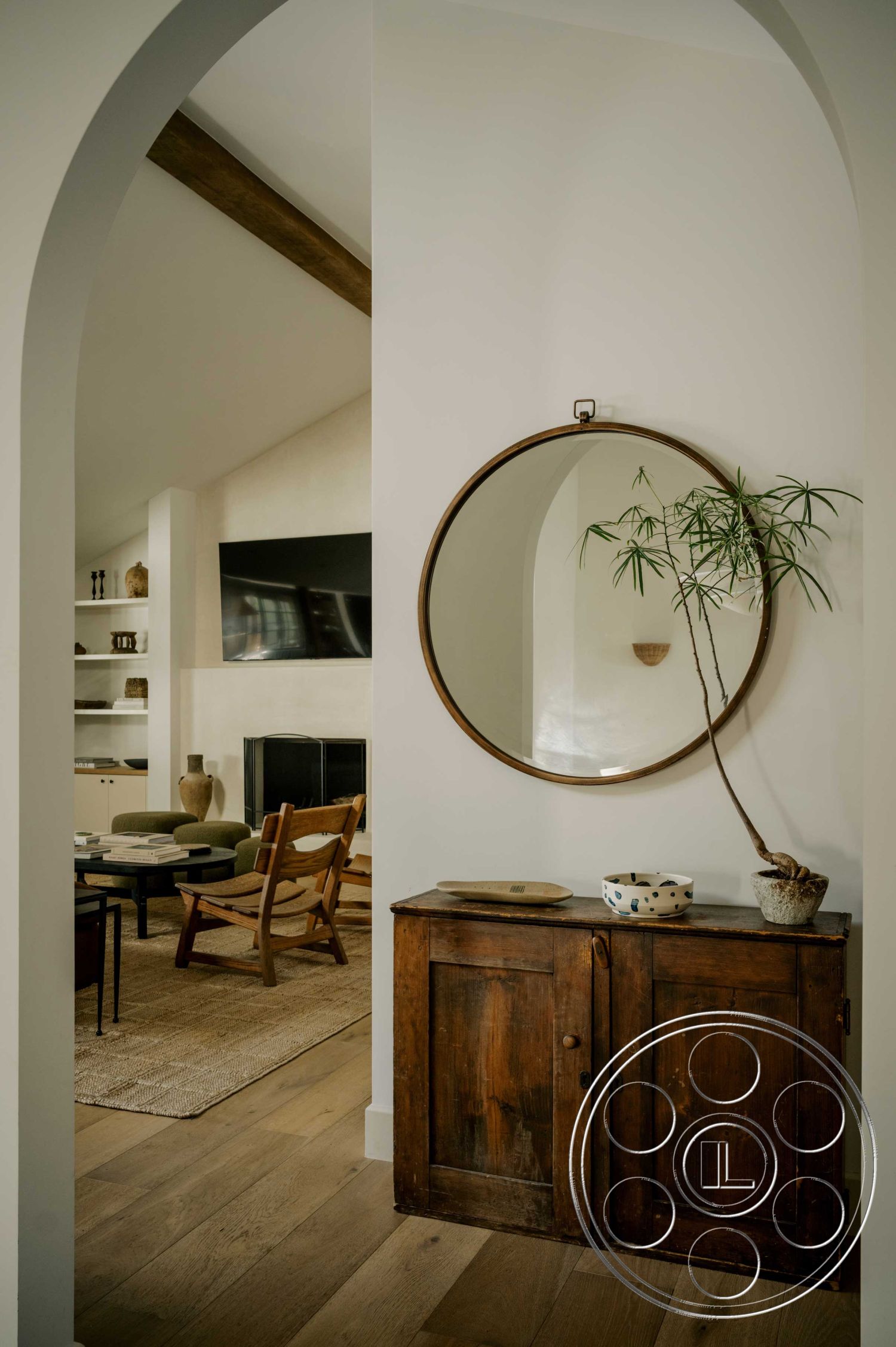 Americana 429 - interior hardwood flooring, interior exposed wood ceiling beams, interior open concept layout, interior white painted walls, interior modern furniture, interior woven area rug, interior round mirror, interior arched doorway, interior wooden accent cabinet, interior houseplant decor, interior dark wood accents, interior modern living room layout