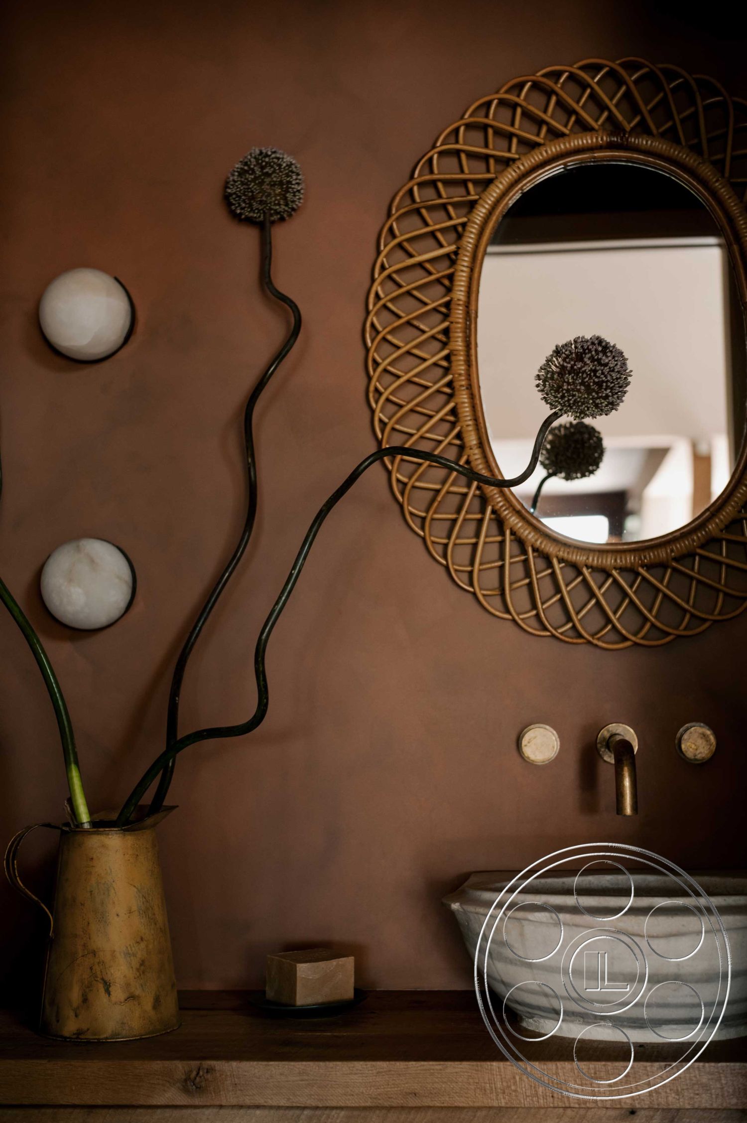 Americana 429 - minimalist design aesthetic interior, textured wall finish interior, exposed clay wall treatment interior, marble vessel sink countertop interior, brass faucet hardware interior, round framed mirror with woven detail interior, wooden floating shelf interior, monochromatic decor accents interior, minimalist vase with botanical elements interior, natural wood tones and materials interior, dim lighting with ambient fixtures interior, ceramic soap dish interior, organic shapes and forms interior