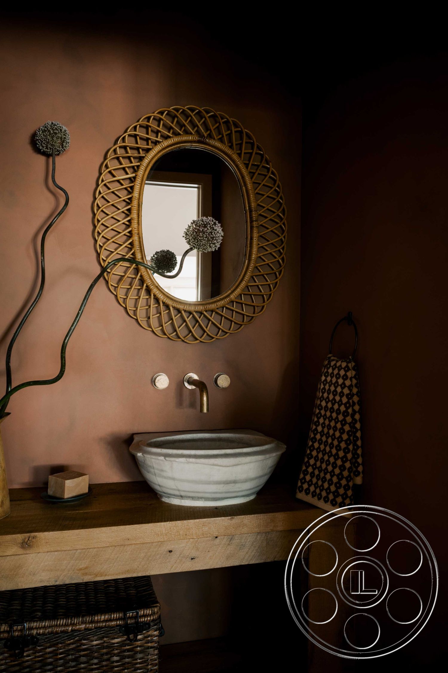Americana 429 - minimalist aesthetic, ambient lighting, interior bathroom design, textured plaster wall treatment, wooden vanity countertop, marble vessel sink, round woven mirror, gold finish faucet, natural fiber basket storage, decorative towel hanging, soft earth-toned color palette, organic shape elements, botanical accent decor, rural farmhouse style