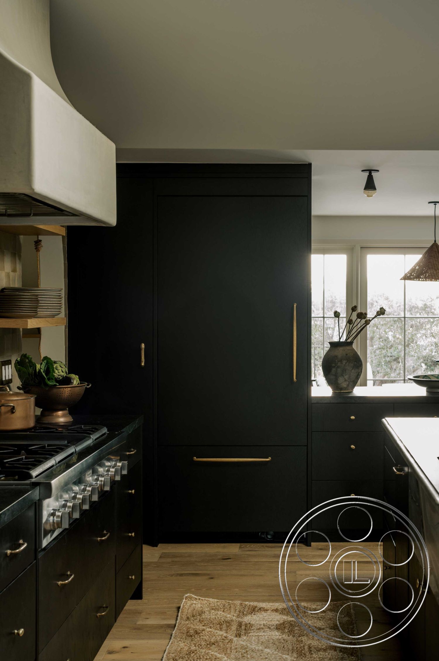 Americana 429 - neutral color palette, textured area rug, stainless steel appliances, window with natural light, modern kitchen island, functional kitchen layout, interior kitchen design, hardwood kitchen floors, gold hardware details, black kitchen cabinetry, concrete range hood, open shelving with ceramic plates, minimalistic decor elements, plant accents in kitchen