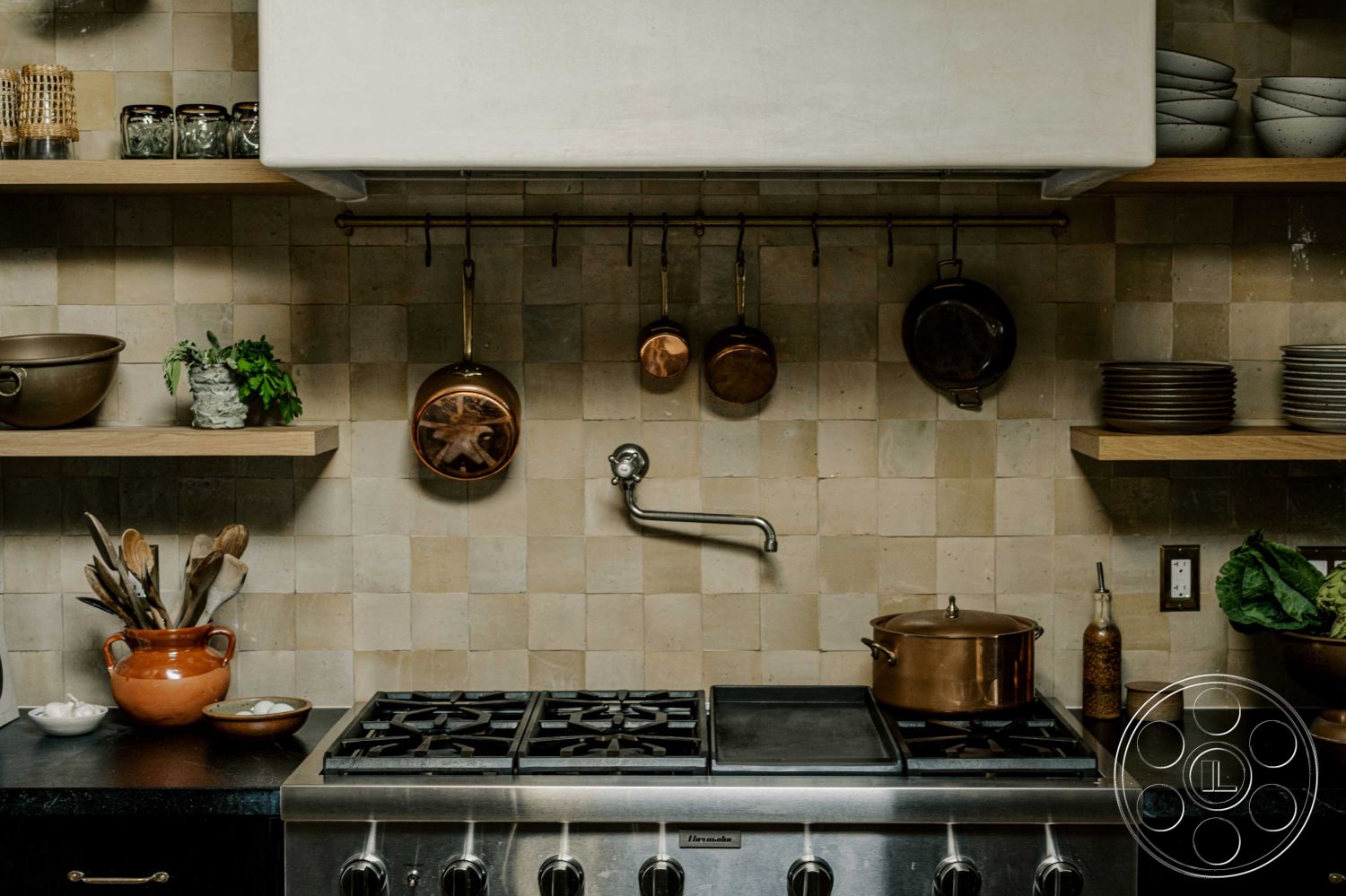 Americana 429 - black granite countertop, interior kitchen design, textured plaster wall treatment, natural stone tile backsplash, open wooden shelving, brass hanging pot rack, copper cookware displays, stainless steel gas stovetop, decorative ceramic bowl, multiple kitchen utensils, urban modern kitchen, minimalist kitchen style, natural light kitchen ambiance