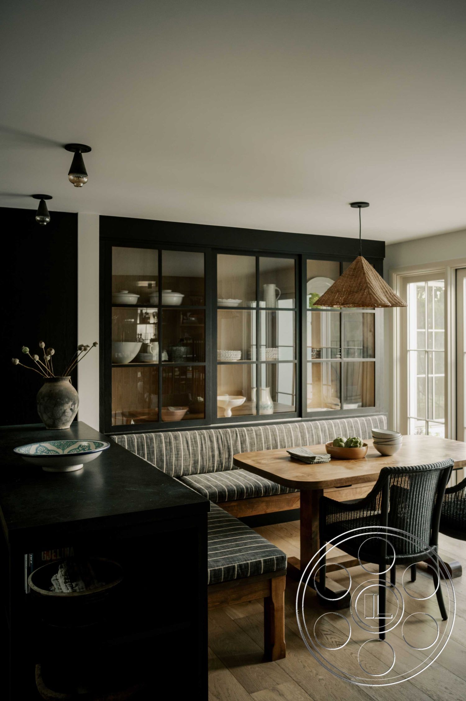 Americana 429 - neutral color palette, hardwood flooring, minimalist design, open concept layout, wood dining table, pendant lighting, large windows for natural light, black cabinetry, textured wall treatment, modern farmhouse style, interior dining area, cozy dining nook, glass-fronted display cabinets, striped fabric banquette seating, ceramic dinnerware display