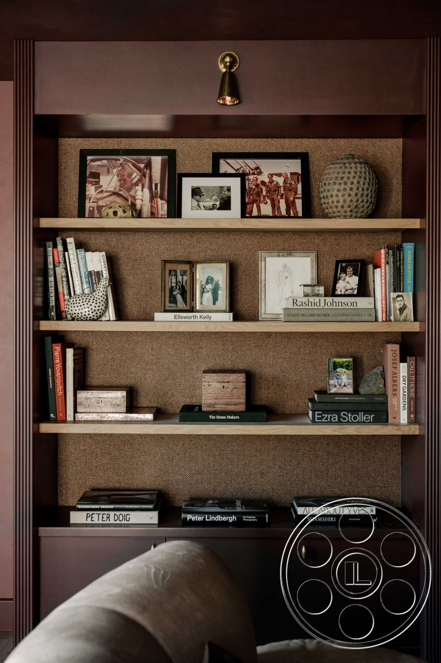 Americana 429 - dark wood cabinetry, textured accent wall, warm color palette, exposed wood shelving, modern decorative vase, minimalist book display, walnut wood shelves, woven textile wall treatment, contemporary interior lighting, photographic art framed displays, designer coffee table books, soft upholstery couch, stylish decorative objects, urban living room, open plan interior design, artistic home office area