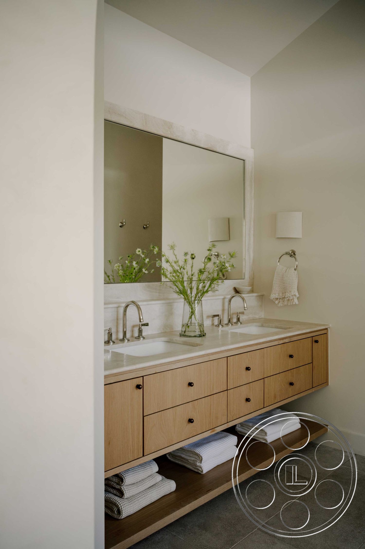 Americana 429 - ceramic tile flooring, white marble countertop, natural light from window, wall-mounted mirror, dual sink vanity, interior bathroom design, modern minimalist aesthetic, neutral painted walls, brushed nickel faucets, light wood vanity cabinet, textured white bath towels, open shelving for towels