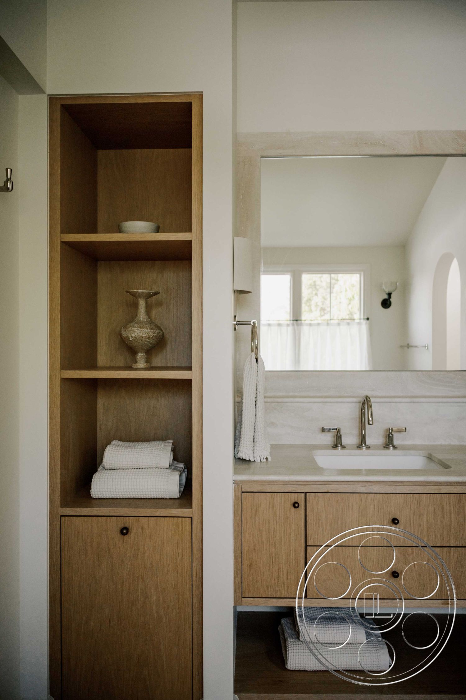 Americana 429 - neutral color palette, spa-like atmosphere, natural light from windows, minimalist interior design, white painted walls, floor-to-ceiling window view, brushed gold faucet fixtures, marble bathroom countertop, rectangular mirror above sink, oak built-in shelving unit, textured linen towels, light wood vanity cabinetry, open shelving with decorative vase, soft bath linens storage, clean-lined bathroom layout, modern fixture accents