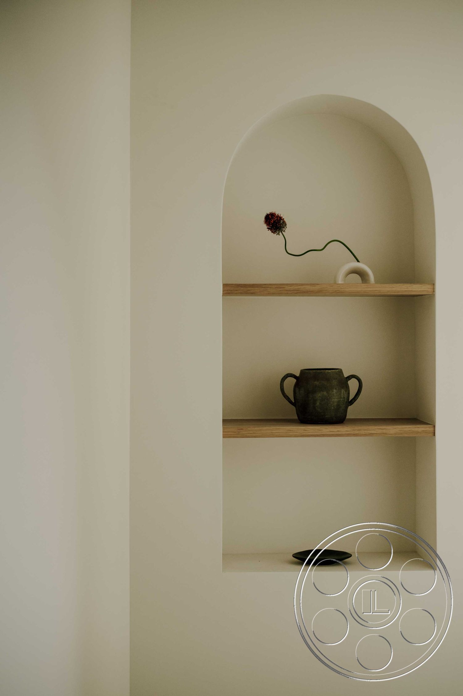 Americana 429 - neutral color palette, textured wall treatment, plaster wall finish, minimalist decor accents, interior shelving niche, arched niche with oak shelf, ceramic vase on shelf, wooden shelf construction, artistic flower arrangement, geometric pottery design