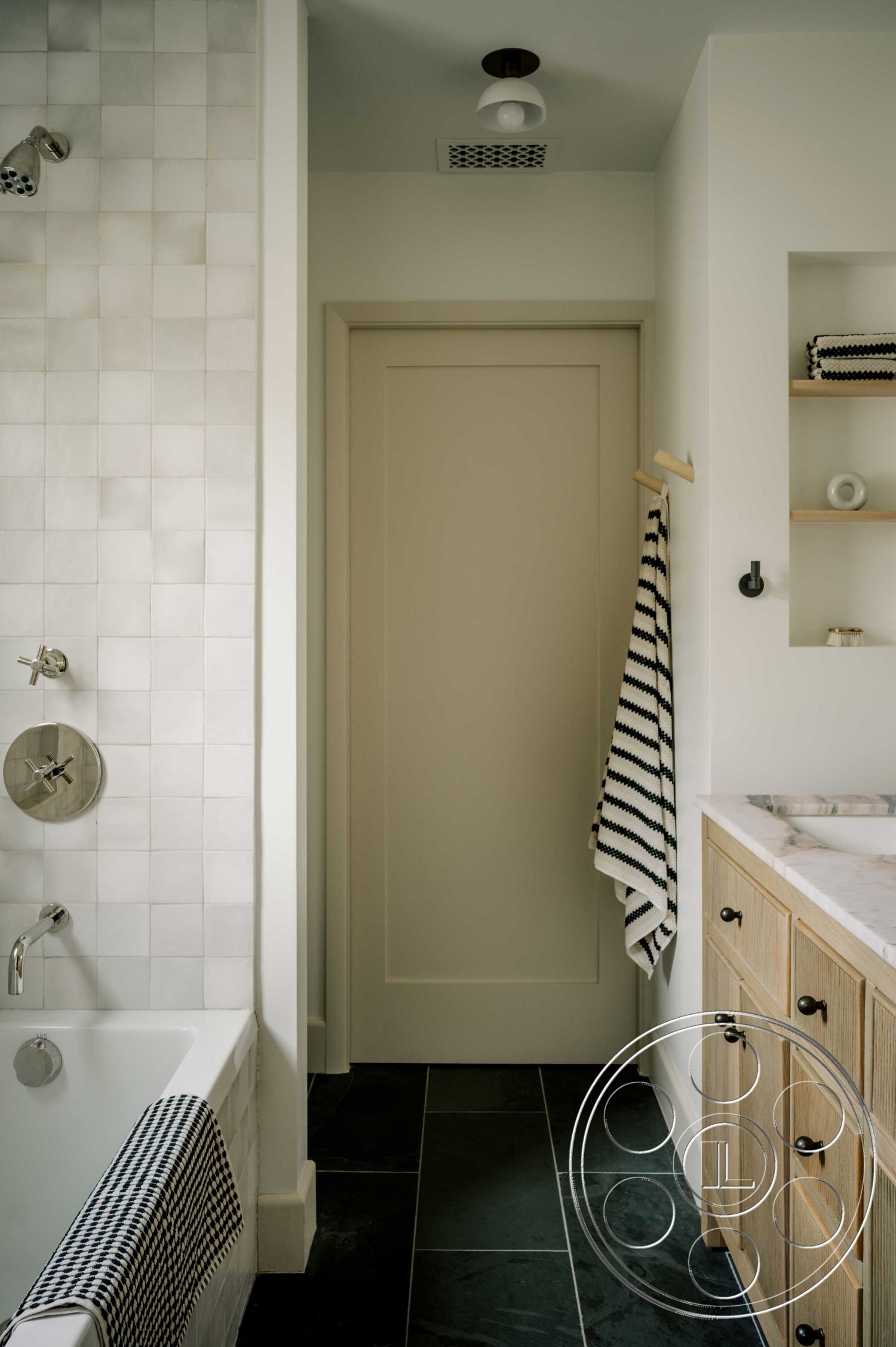 Americana 429 - neutral color palette, minimalist design, black slate flooring, interior bathroom, marble countertop sink, open shelving for storage, functional bathroom layout, white glossy tile shower walls, wood vanity with natural finish, modern brushed nickel fixtures, plain white door, striped towel hanging