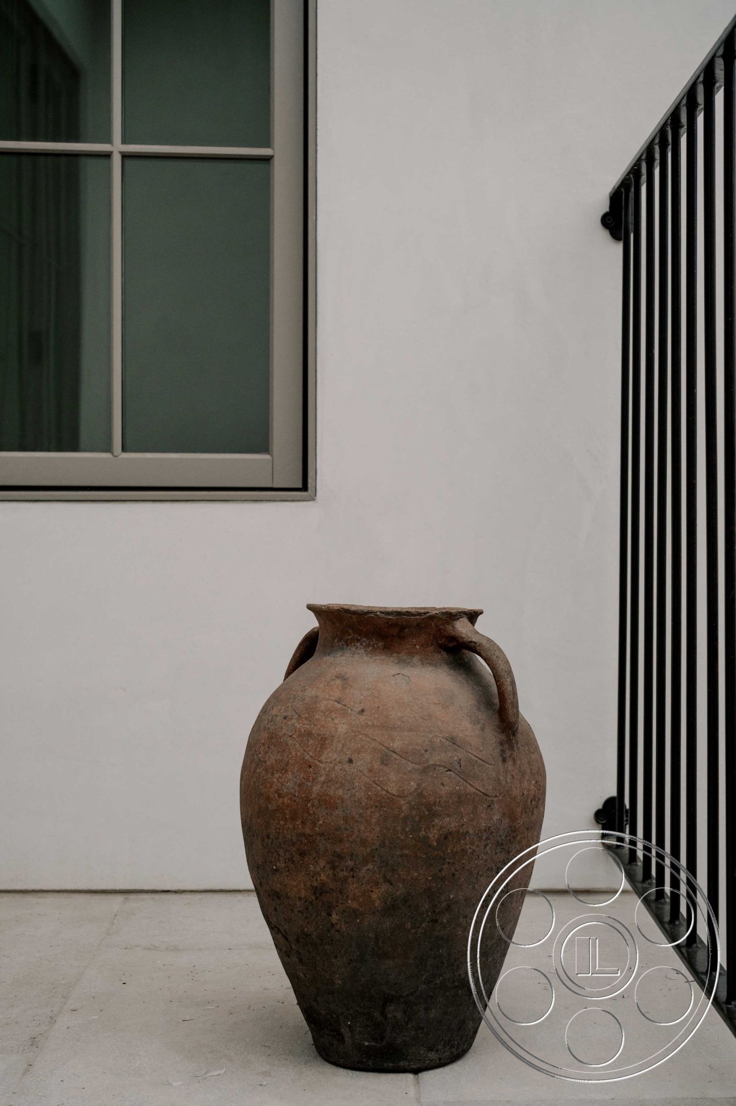 Americana 429 - neutral color palette, architectural simplicity, textured plaster wall treatment, natural light infusion, clean lines and shapes, smooth concrete patio floor, terra cotta pottery vase, black metal railing details, rectangular window frame, modern minimalistic exterior, interior garden setting, traditional pottery accent