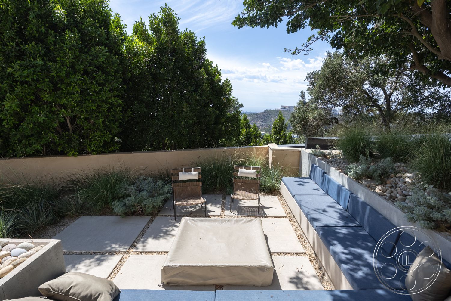 Modern 511 - natural stone accents, exposed concrete walls, lush greenery backdrop, concrete patio flooring, minimalist garden design, rectangular patio seating area, low-profile outdoor seating, textured stone flowerbed edges, gravel landscape detailing, modern outdoor lounge, planter box with smooth river stones, framed mountain view, casual outdoor living space, interior outdoor flow