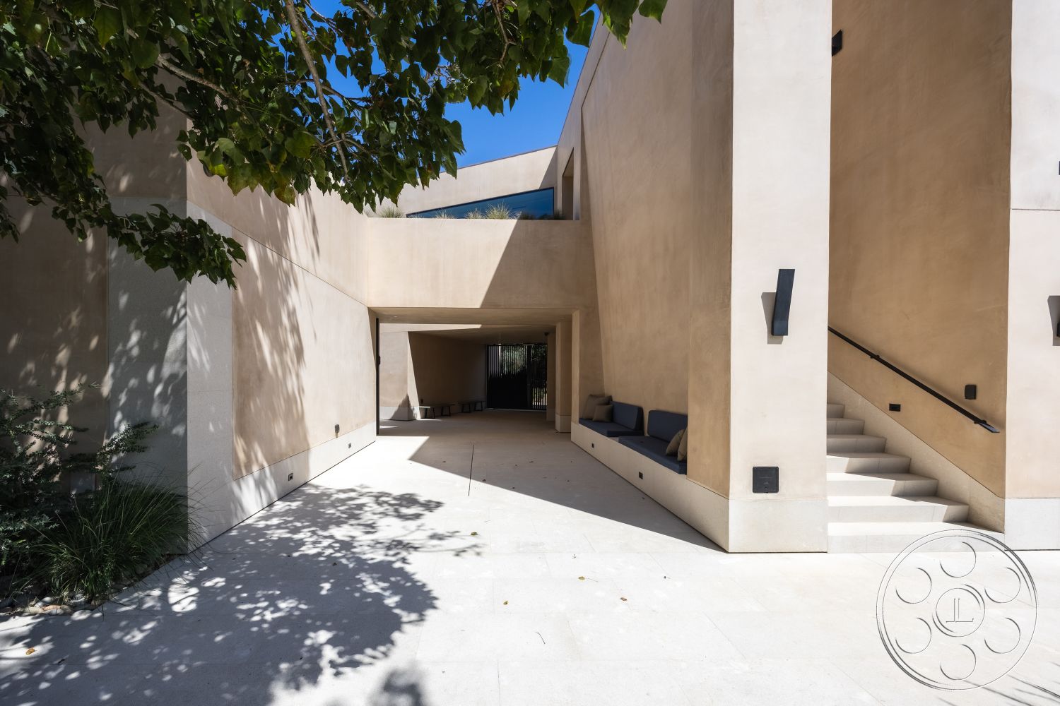 Modern 511 - contemporary architectural style, wood bench seating, natural stone patio flooring, open courtyard design, exterior plaster walls, modern straight staircase, glass accent window, concrete steps leading to entrance, structured landscape with low greenery, minimalist entrance area, indoor-outdoor flow design, soft natural light illumination, integrated outdoor living space, urban setting with foliage