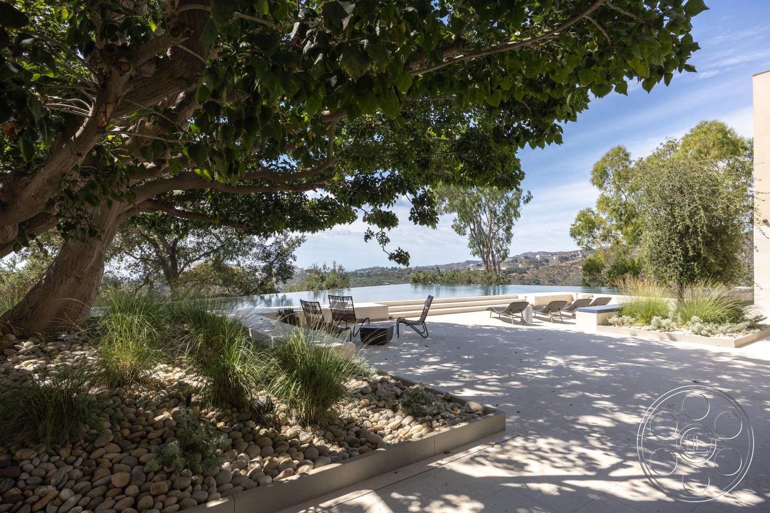 Modern 511 - contemporary architectural style, exterior concrete patio flooring, infinity pool with concrete pool border, natural stone landscaping elements, oversized reclining lounge chairs, lush grass planting beds, surrounding natural tree canopy, smooth pebble ground cover, modern outdoor space with minimalist design, open view of serene lake, sunny outdoor leisure area, level ground patio area