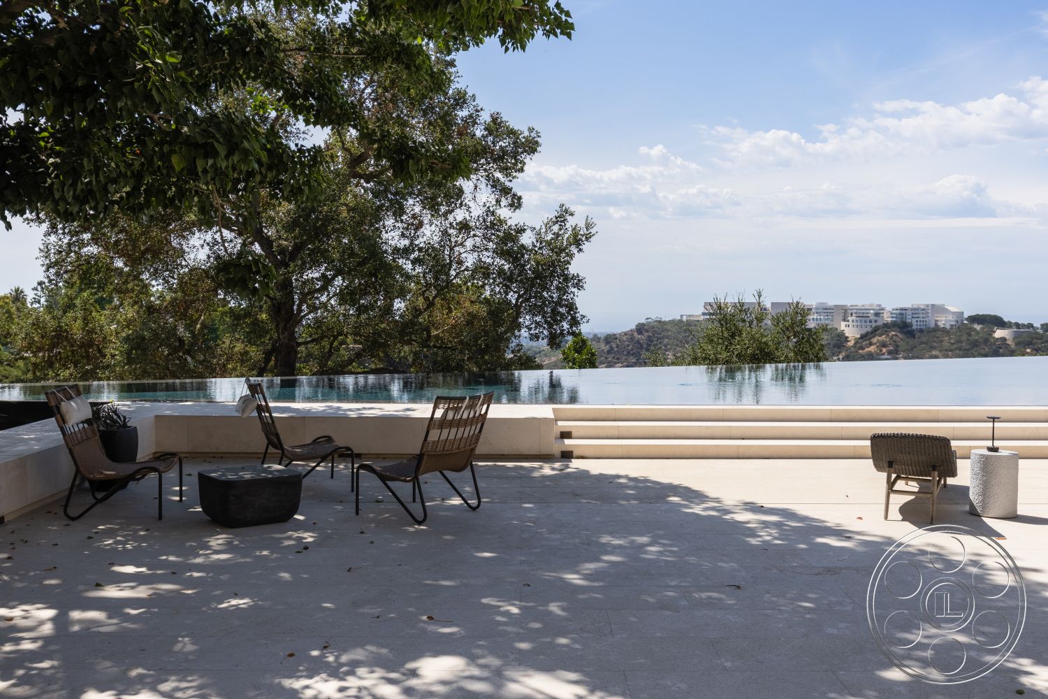 Modern 511 - exterior, textured stone wall, open-air design, modern outdoor seating, minimalist outdoor decor, landscaped garden setting, contemporary outdoor lounge area, concrete pool surround, limestone patio flooring, infinity pool edge, residential hillside property, glass pool barrier, natural shade from trees, panoramic view of city skyline, sun-drenched terrace