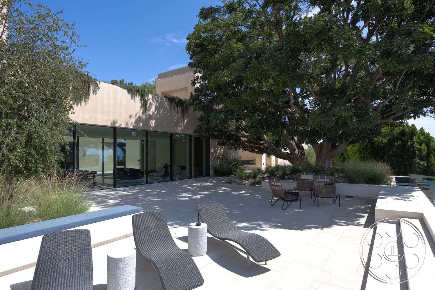 Modern 511 - minimalist aesthetic, large glass sliding doors, urban setting, expansive outdoor space, woven lounge chairs, contemporary home design, modern outdoor seating area, landscaped garden with native plants, exterior concrete patio flooring, large shade tree, textured stucco wall finish, flat roof modern architecture, stone planter beds, pool area with adjacent patio