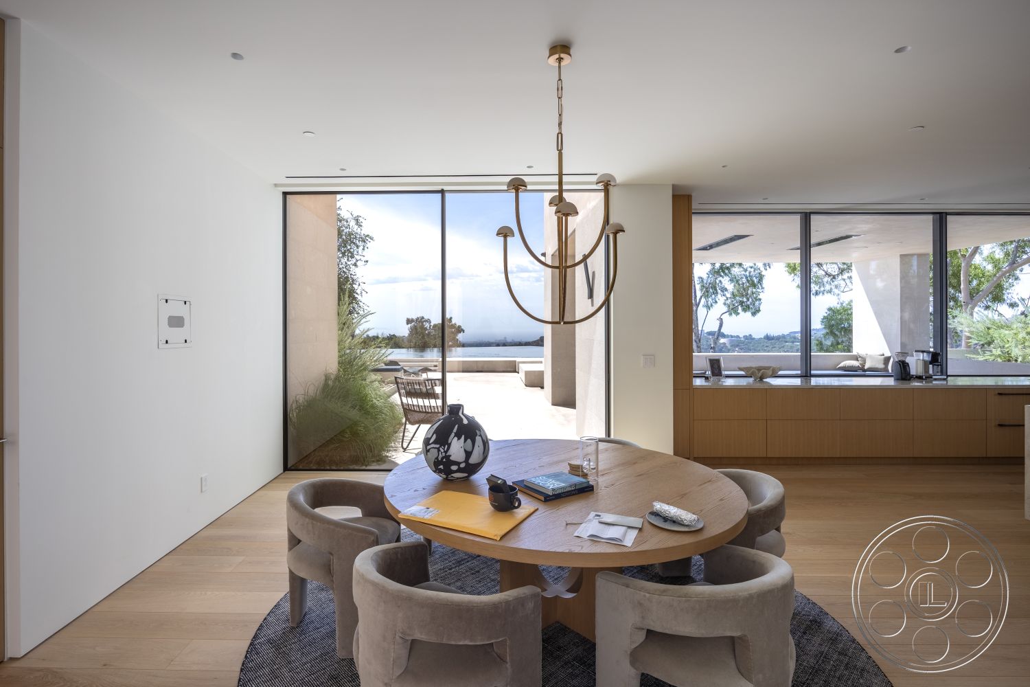 Modern 511 - neutral color palette, minimalist design elements, upholstered dining chairs, floor-to-ceiling windows, round dining table, contemporary architectural style, interior dining space, smooth plaster walls, hardwood dining room floors, modern chandelier light fixture, open-plan layout interior, natural light dining area, warm wood cabinetry, outdoor view through glass sliders, adjacent outdoor patio, set in a hillside location, lush landscaping outside