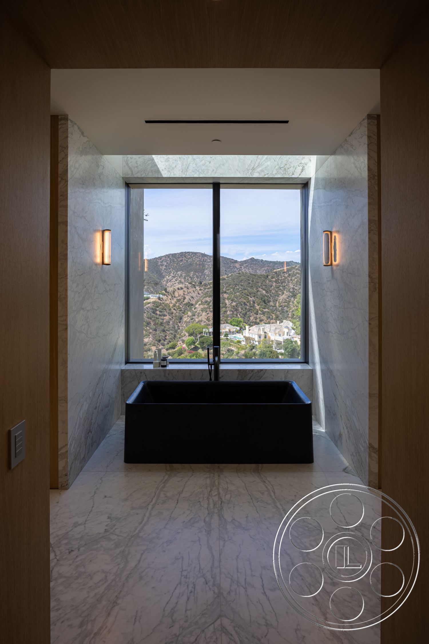 Modern 511 - neutral color palette, contemporary light fixtures, urban hillside location, minimalist design aesthetic, functional bathroom space, modern bathroom layout, natural light ambiance, luxurious spa-like atmosphere, interior bathroom with marble wall treatments, black freestanding soaking tub, white marble flooring with grey veining, floor-to-ceiling window with mountain view, wood ceiling detail, large panoramic window, exposed stone wall feature, geometric tub shape