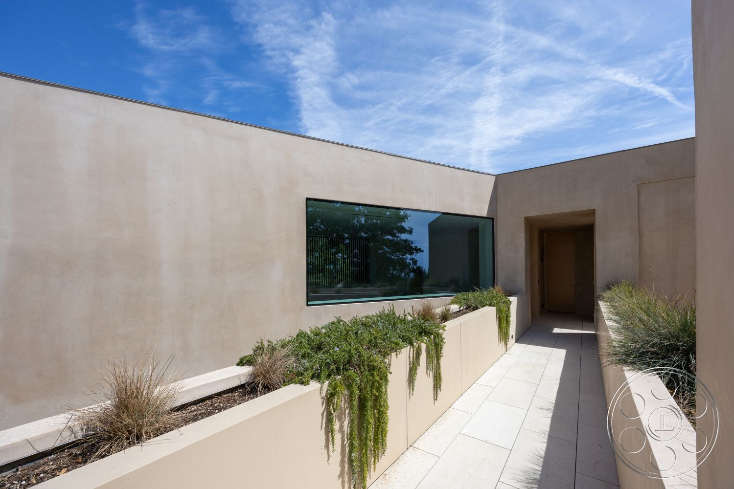 Modern 511 - urban setting, concrete walkway, soft earth tones, sunlit pathway, flat roof design, exterior stucco walls, contemporary home design, minimalist architectural style, natural light emphasis, large glass window, clean lines and angles, horizontal window design, rectangular planters with greenery, modern outdoor landscaping, open-air entrance, dry landscaping features