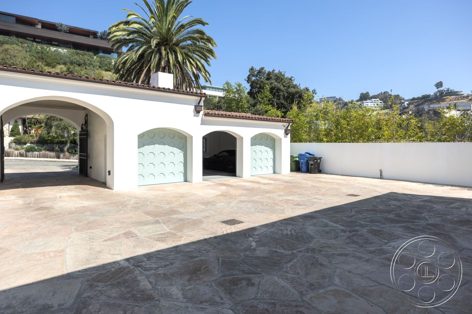 Spanish 168 - exterior, planted greenery, two-car garage, curved driveway, palm trees in background, landscaped garden area, stucco wall finish, natural stone driveway, arched garage openings, paved parking area, tile roof with red clay tiles, modern residential setting, outdoor access pathway