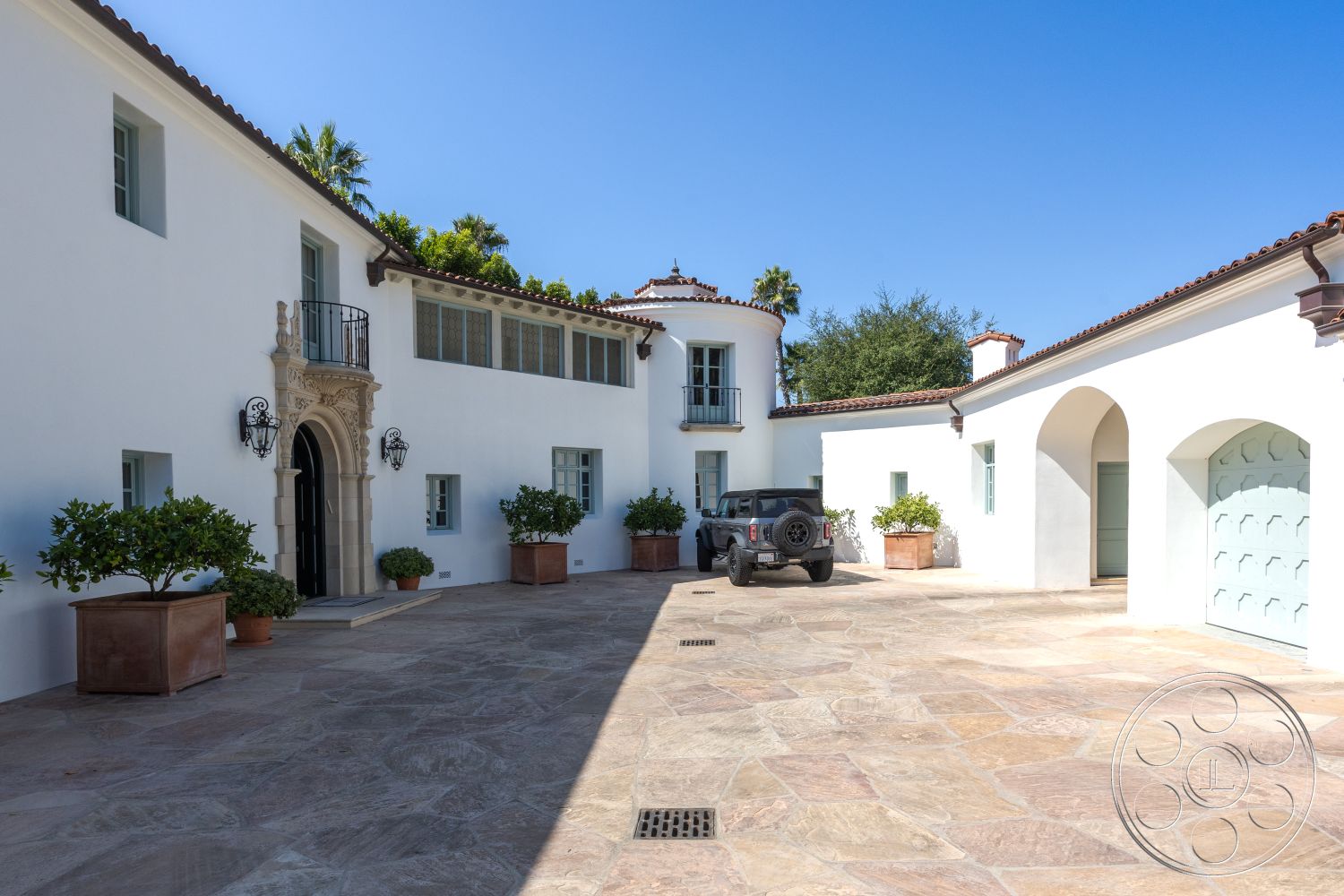 Spanish 168 - exterior, landscaped courtyard, stucco walls, arched doorways, terracotta tile roof, serene environment, decorative wall sconces, tropical greenery, double front doors, modern farmhouse style, urban residential setting, private driveway, stone planter boxes, ample natural light, flagstone driveway, rounded entryway, metal balcony railing, paved patio flooring, southwestern architectural details