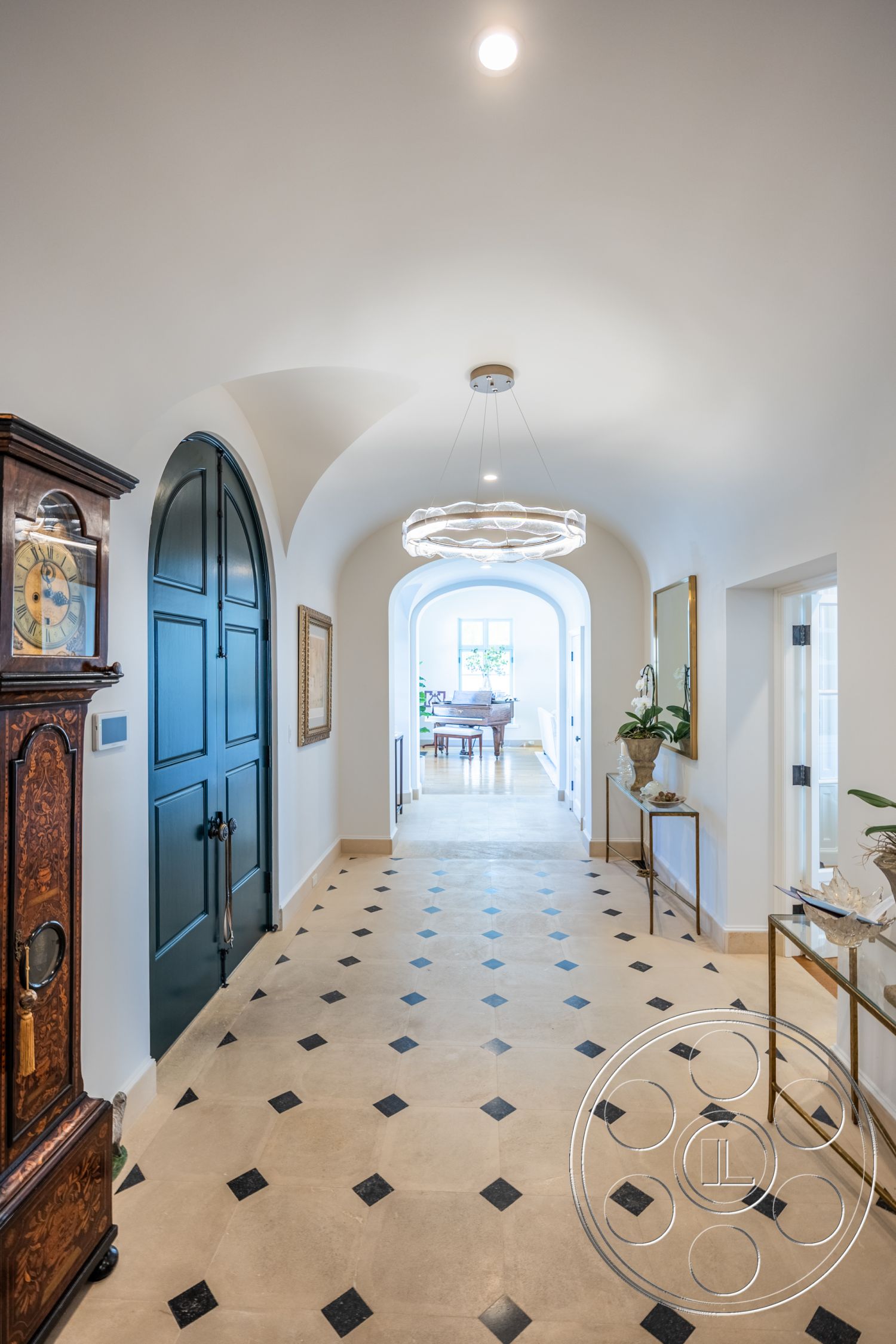 Spanish 168 - high ceilings, polished stone flooring, natural light from large windows, arched doorways, modern chandelier, white plaster walls, stylish console table, lush indoor plants, decorative wall mirrors, dark wood accent pieces, large pendant lighting, hexagonal tile flooring with black accents, open hallway design, decorative artwork frames, traditional wooden clock