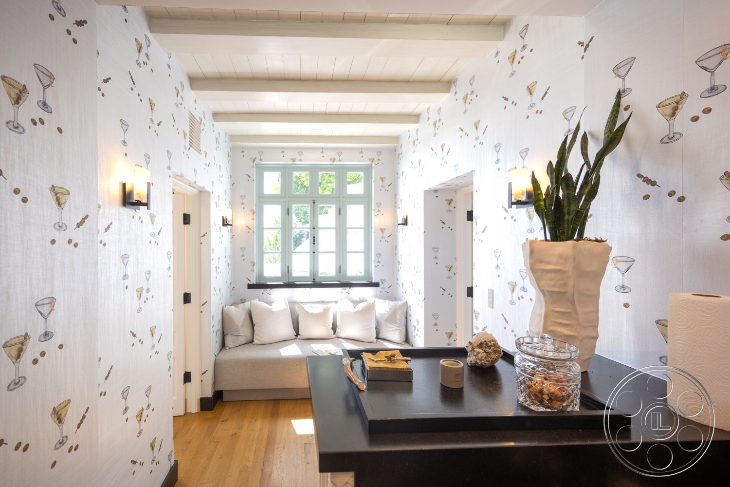 Spanish 168 - light wood ceiling beams, hardwood entryway floors, modern wall sconces, decorative stone accents, textured wallpaper with martini design, built-in couch with throw pillows, ceramic planter with greenery, black countertop with decorative items, natural light from double-hung windows