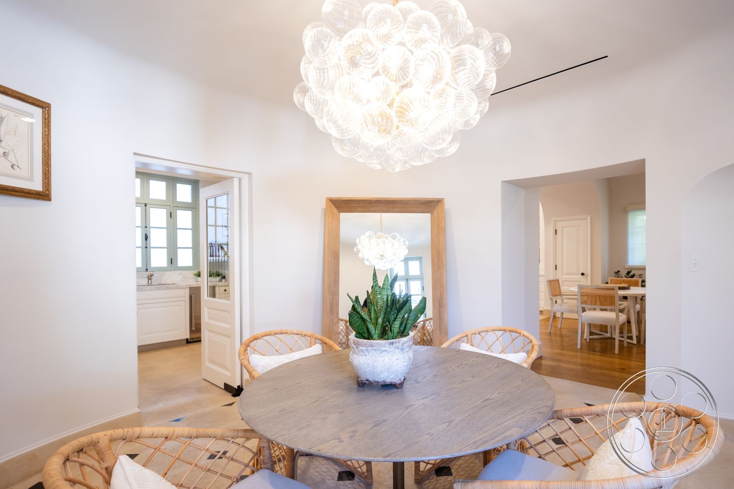 Spanish 168 - minimalist decor, neutral color palette, modern furnishings, natural wood flooring, open-plan layout, light-filled space, interior dining area, glass pendant light fixture, large decorative mirror, arched doorways leading to kitchen, textured white walls, circular wood dining table, rattan dining chairs, veneer wood tabletop, indoor plant centerpiece, kitchen access doorway