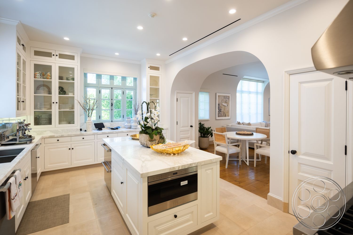 Spanish 168 - interior kitchen design, suburban home interior, soft natural lighting from large windows, minimalist kitchen style, marble countertop kitchen island, white cabinetry kitchen, open concept kitchen and dining area, light beige tile flooring, arched doorway between kitchen and dining area, floor-to-ceiling windows in dining area, glass-front cabinetry, modern stainless steel appliances, decorative plants for kitchen decor, classic white door with black hardware, tasteful kitchen decor elements, casual dining area with round table, elegant interior finishes, textured wall treatment near countertop