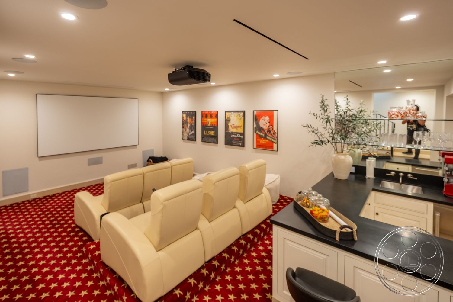 Spanish 168 - open concept design, glassware display, black granite countertop, ceiling-mounted projector, white painted walls, modern track lighting, sound system speakers, cozy entertainment space, interior home theater room, beige leather reclining chairs, carpet with red star pattern flooring, projector screen wall, decorative movie posters, white cabinetry in bar area, functional bar setup